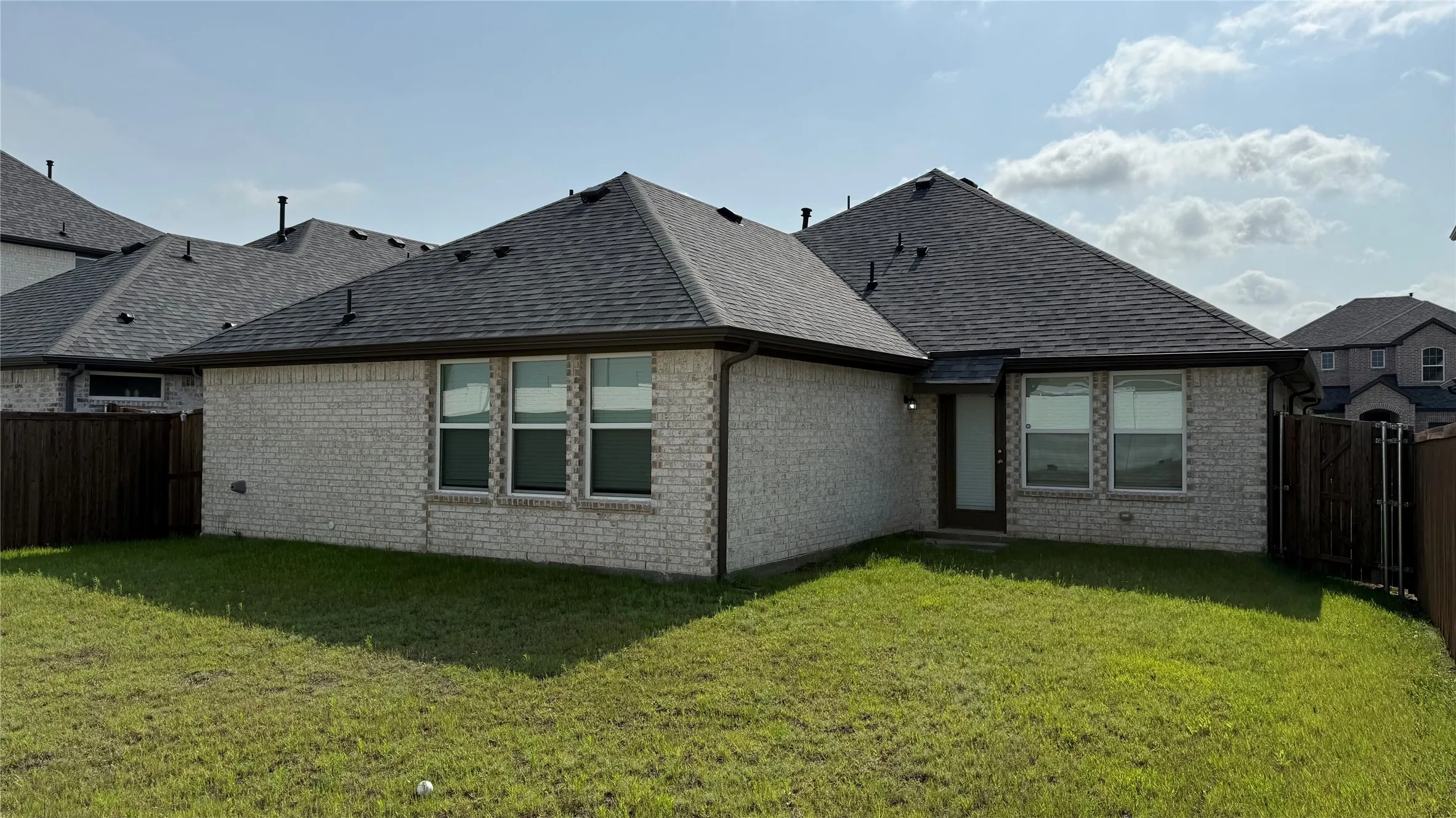 Rear exterior featuring light-colored brick siding, a dark shingle roof, and multiple windows