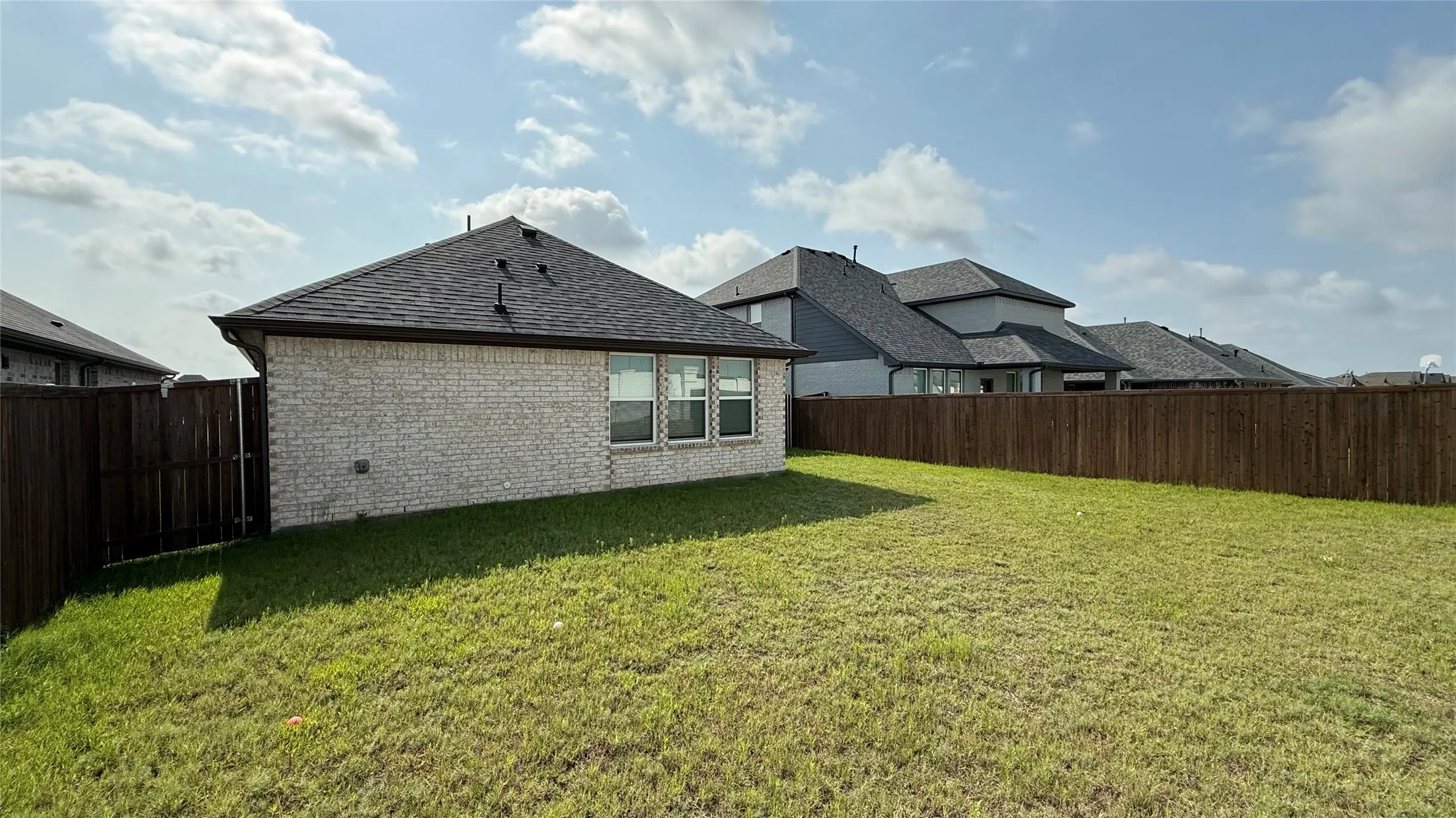 Spacious backyard featuring a grass lawn, privacy fencing, and a light-colored brick exterior with multiple windows