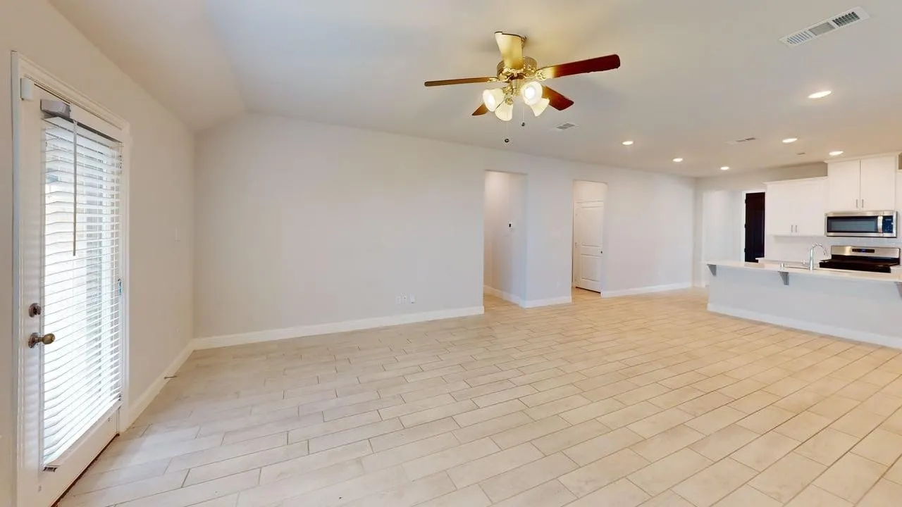 Open-concept living area featuring tile flooring, vaulted ceilings, and a ceiling fan with integrated lighting