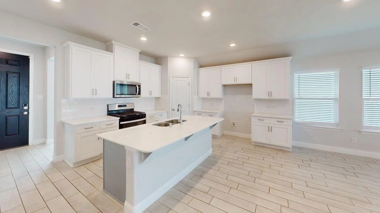 Open-concept kitchen featuring an island with a dual-basin sink, white shaker cabinetry, stainless steel appliances, and white subway tile backsplash