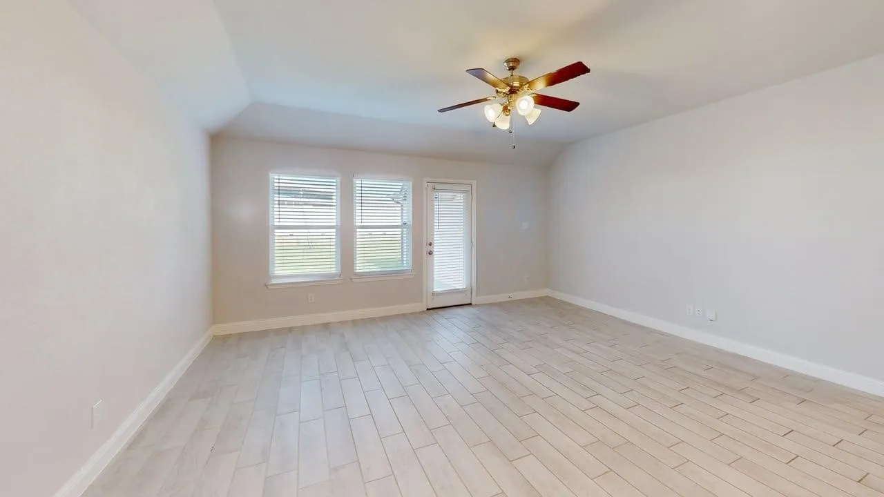 Spacious interior room featuring light wood-finish flooring, a vaulted ceiling, and a ceiling fan with integrated lighting