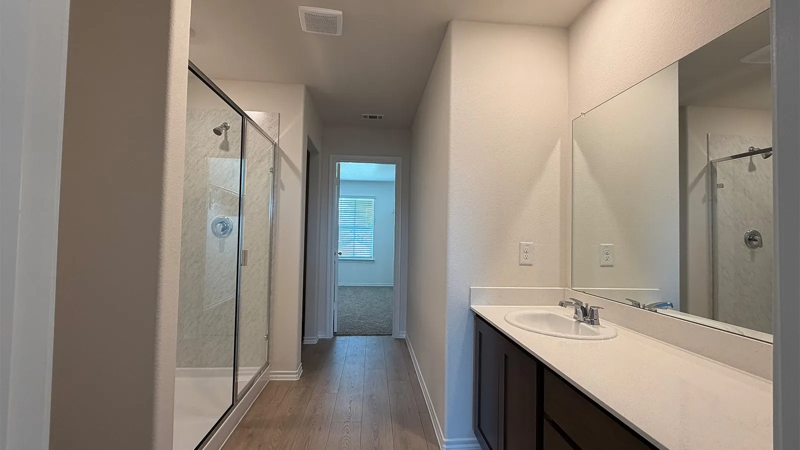 Bathroom featuring a glass-enclosed shower, a vanity with a white countertop and integrated sink, a large wall-mounted mirror, wood-finish flooring, and light-toned walls