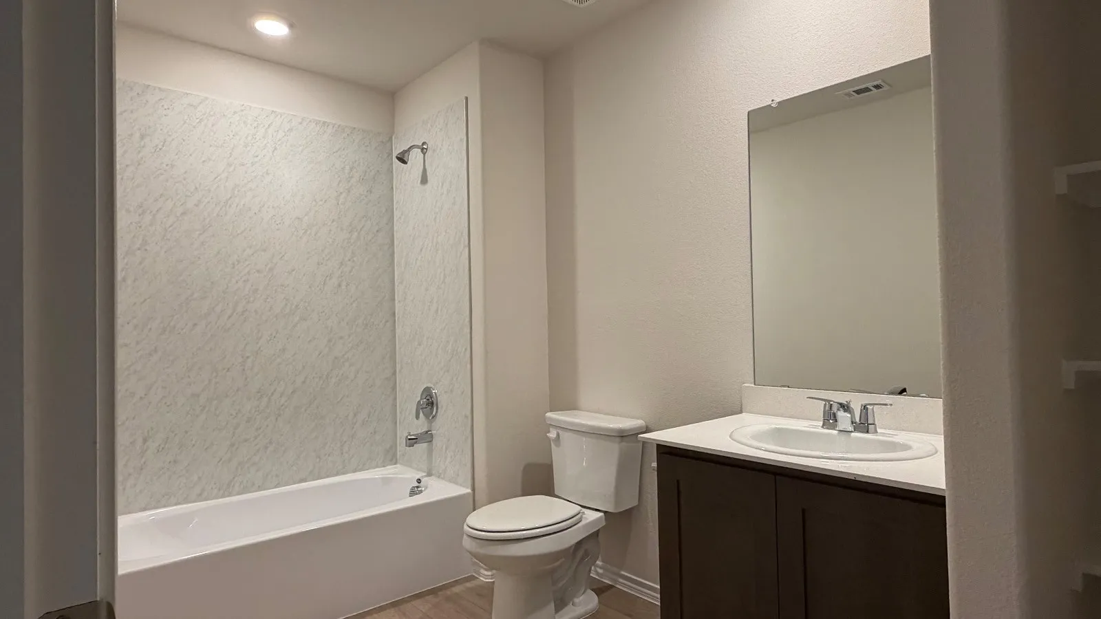 Bathroom featuring a white tub with patterned surround, chrome fixtures, a dark wood-finish vanity with a single sink, light-toned countertop, and an unframed mirror