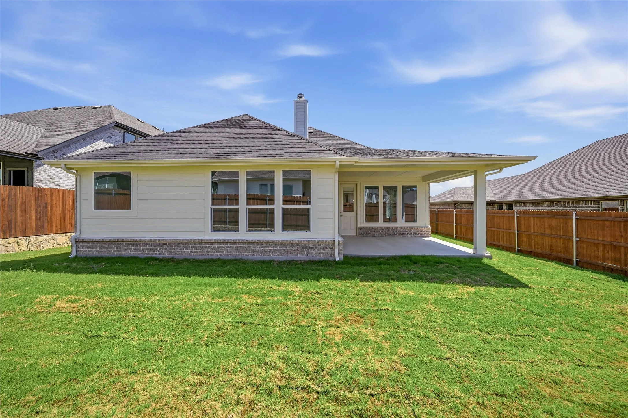 Expansive rear yard with a covered patio, multiple large windows, and a chimney feature