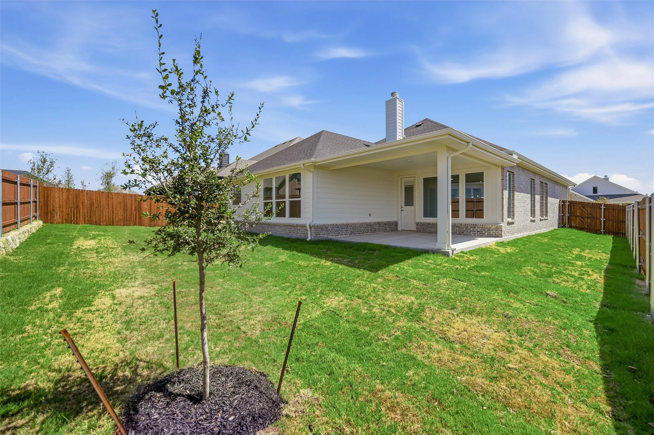 Expansive backyard with a covered patio, manicured lawn, and privacy fencing