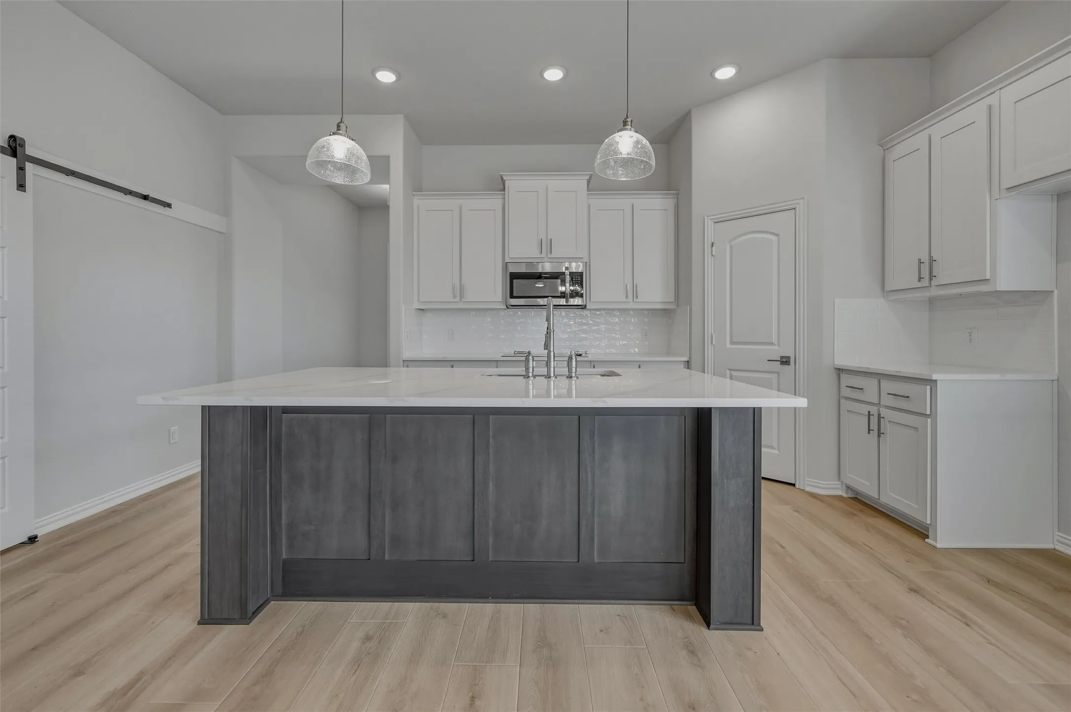 Kitchen island with seating, pendant lighting, wood-finish flooring, white cabinetry, and a white tile backsplash
