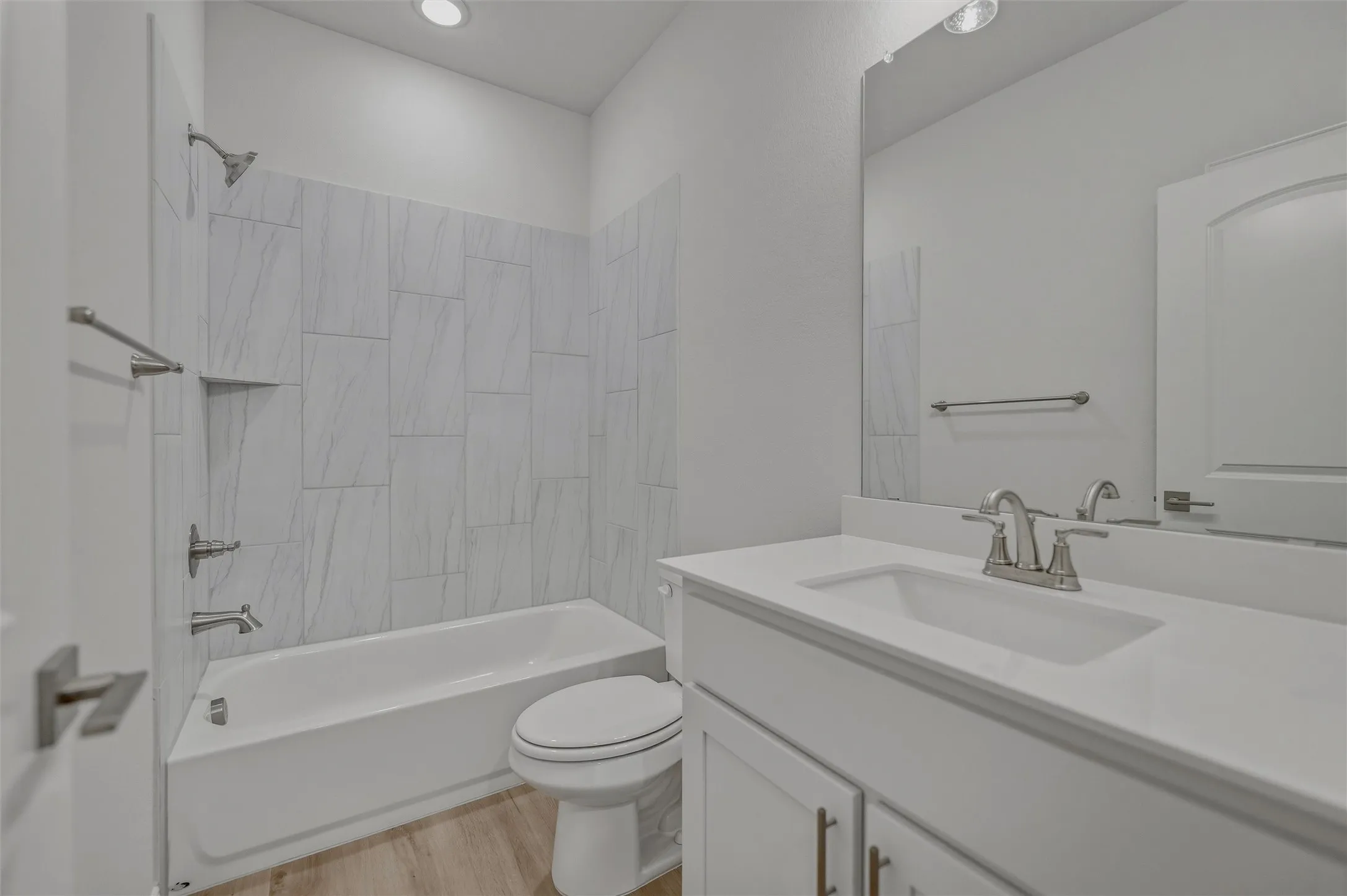 White tub with a tiled shower surround, recessed shower niche, and a brushed nickel showerhead