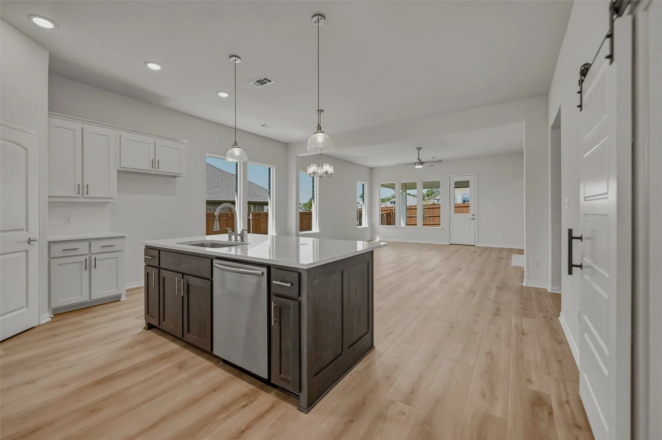 Kitchen island with a built-in sink and stainless steel dishwasher, pendant lighting, wood-finish flooring, white cabinetry, and a barn-style door