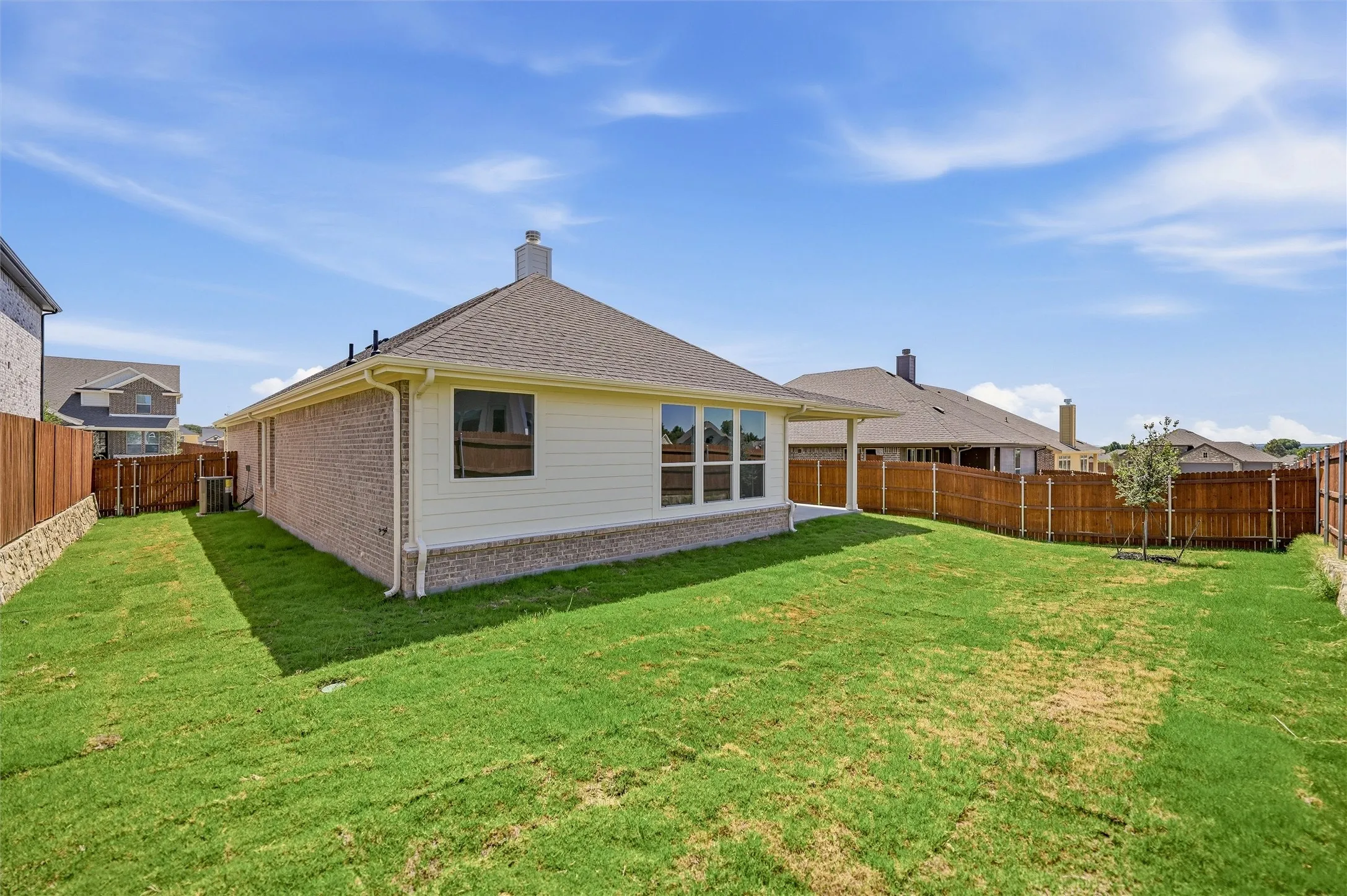 Expansive backyard featuring a manicured lawn, wood fencing, and a covered patio
