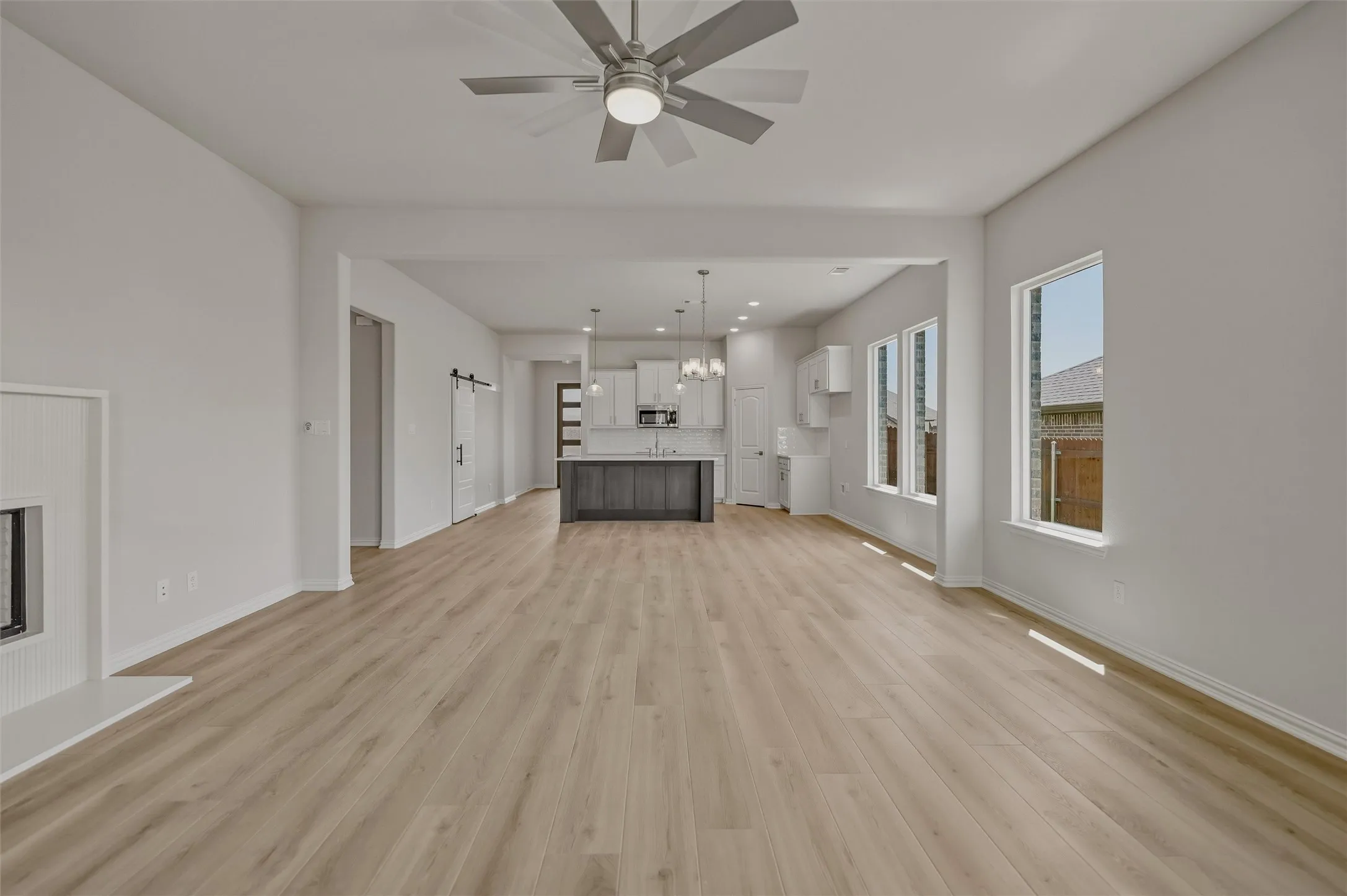 Spacious living area featuring wood-finish flooring, a modern ceiling fan with integrated lighting, and multiple windows