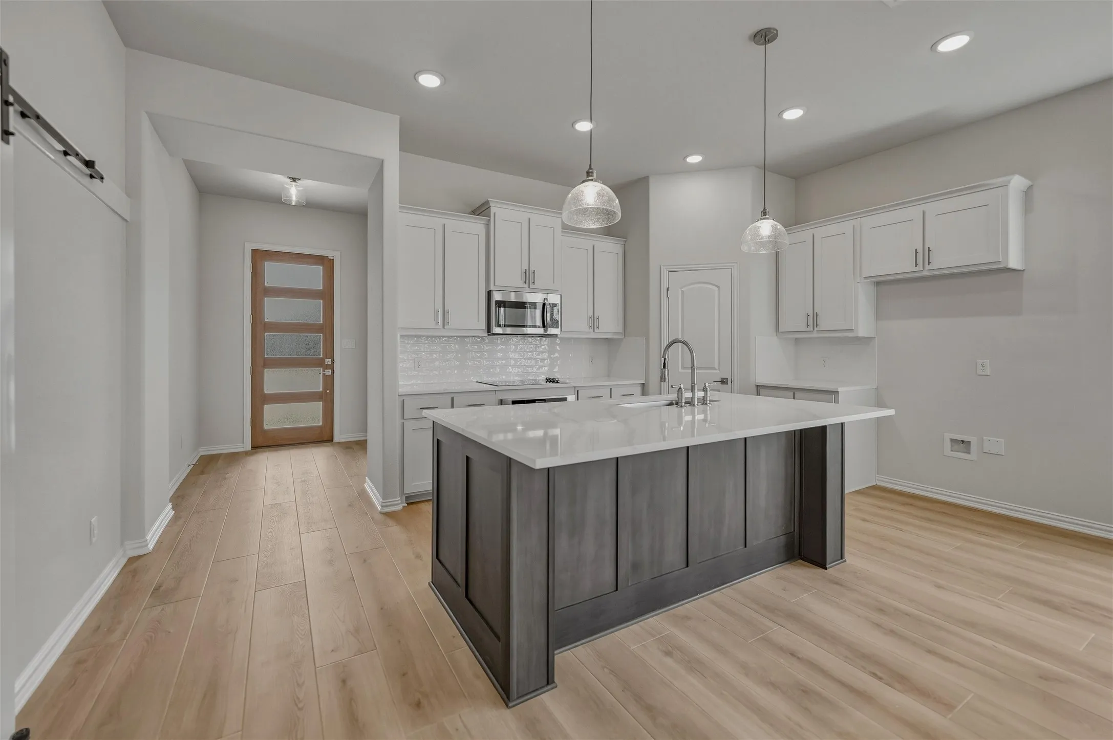 Kitchen featuring a central island with a light-toned countertop, white cabinetry with silver-tone hardware, wood-finish flooring, and recessed ceiling lighting
