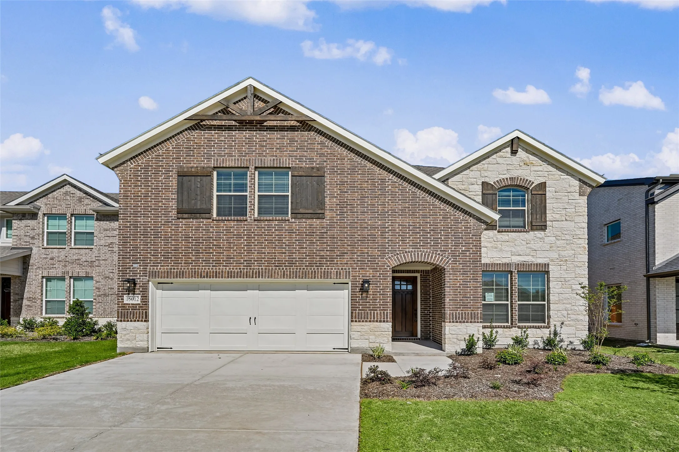 Brick and stone facade, arched entryway, attached two-car garage, manicured lawn, and planted landscaping