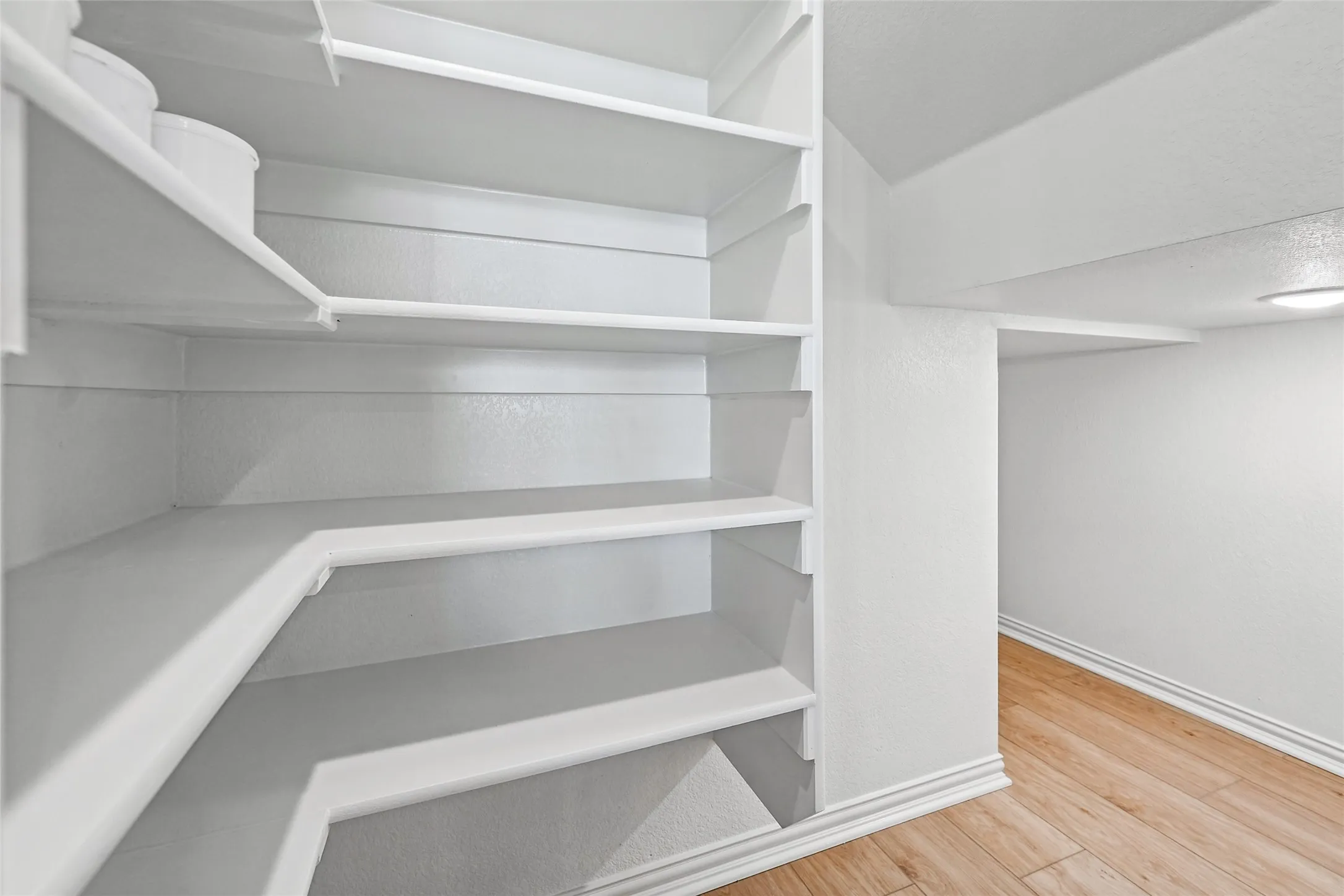 Built-in shelving with multiple levels, white painted walls, wood-finish flooring, and recessed ceiling lighting