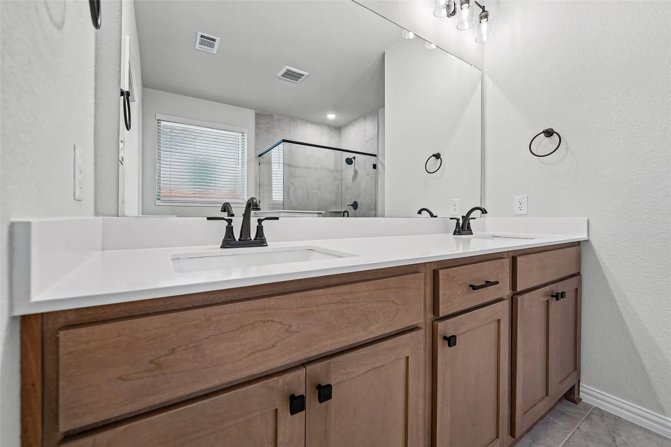 Dual vanity with wood-finish cabinetry, white countertops, and matte black fixtures