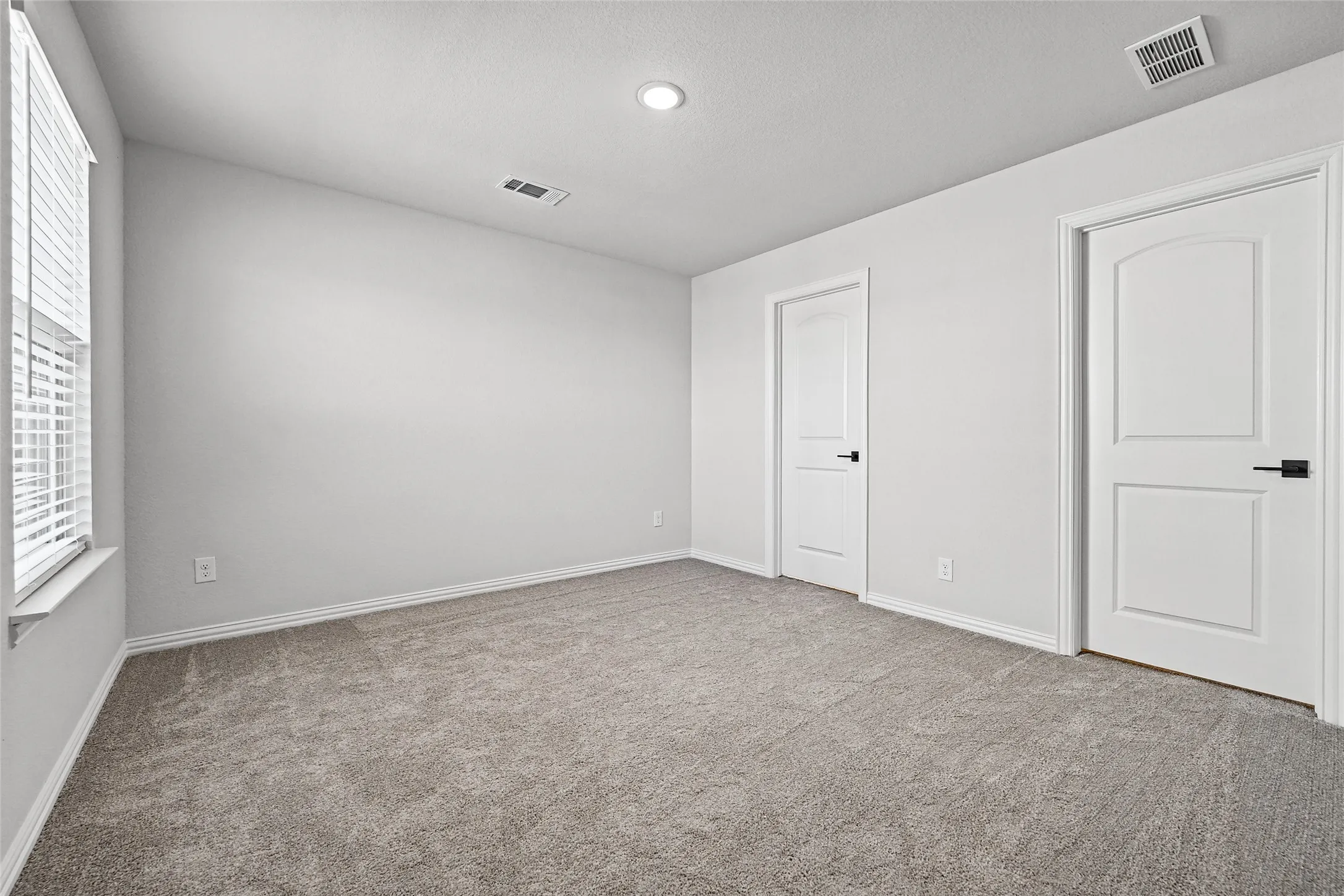 Neutral-toned walls with recessed lighting, two panel doors with matte black hardware, and gray carpet flooring