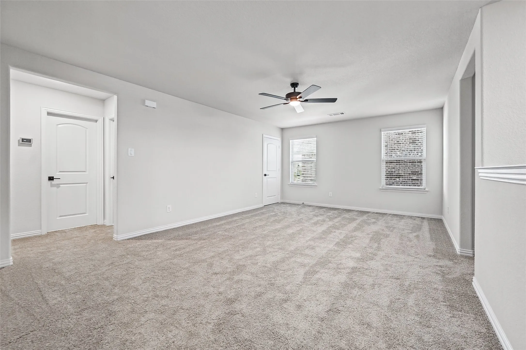 Spacious room with light gray carpet, multiple windows, and a ceiling fan