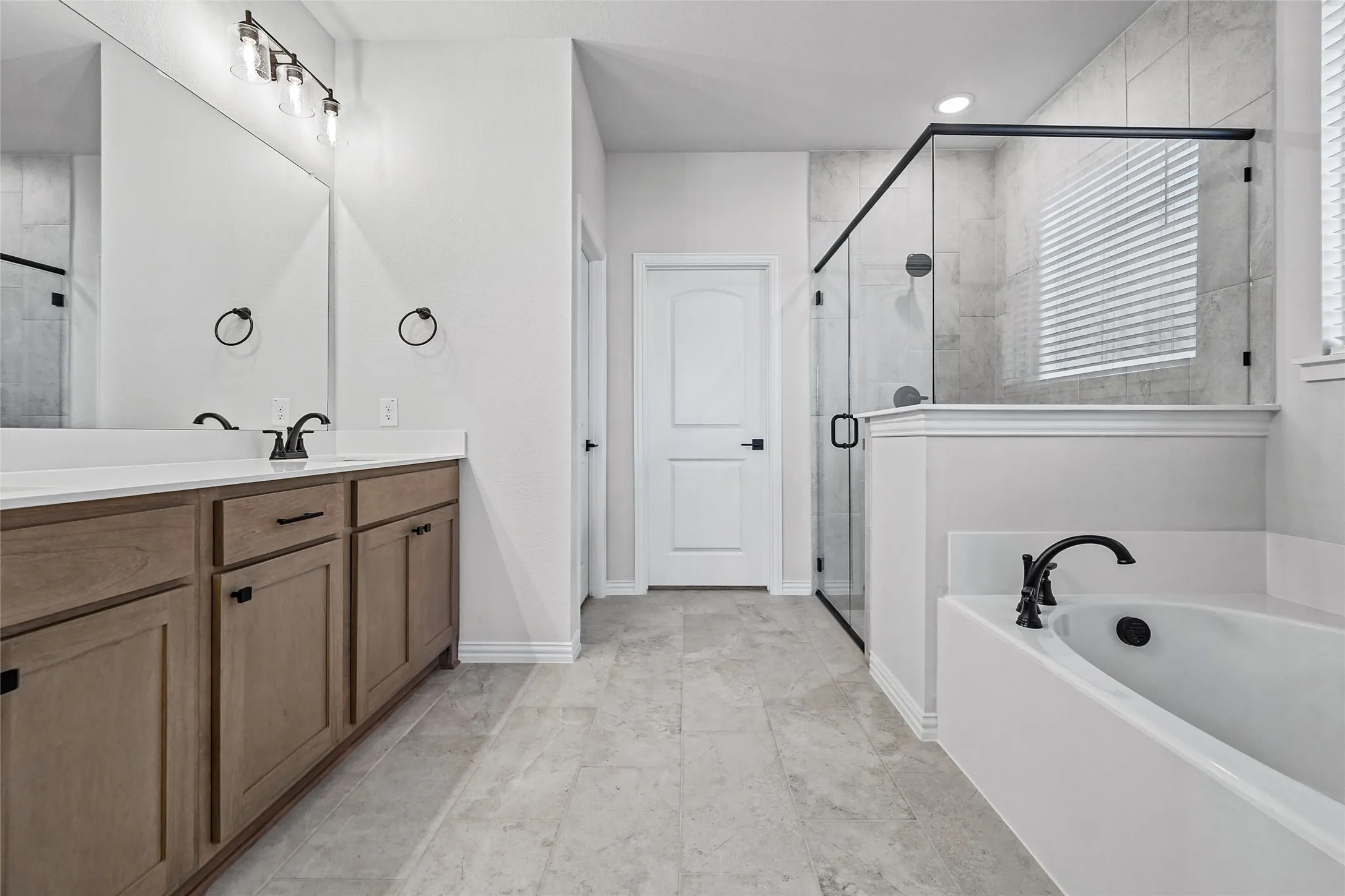 Dual vanity with wood-finish cabinetry, built-in soaking tub, walk-in shower with glass enclosure, and tiled flooring