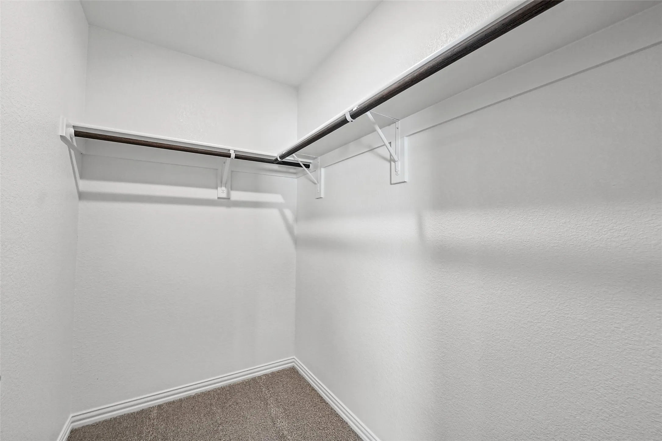 Corner closet with integrated shelving and hanging rods over carpet flooring