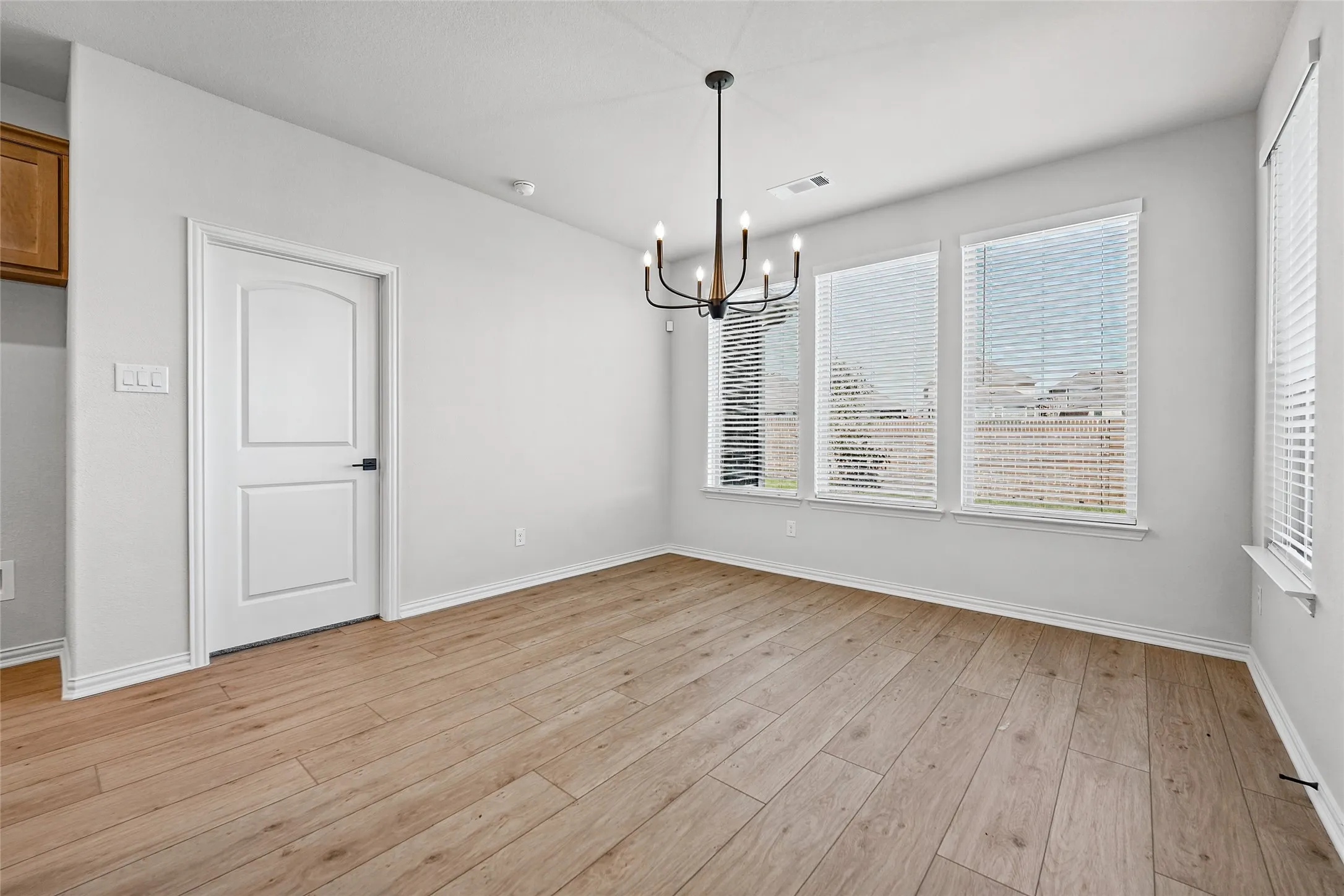 Wood-finish flooring, contemporary chandelier, three large windows, white paneled door with dark hardware, and light-toned walls