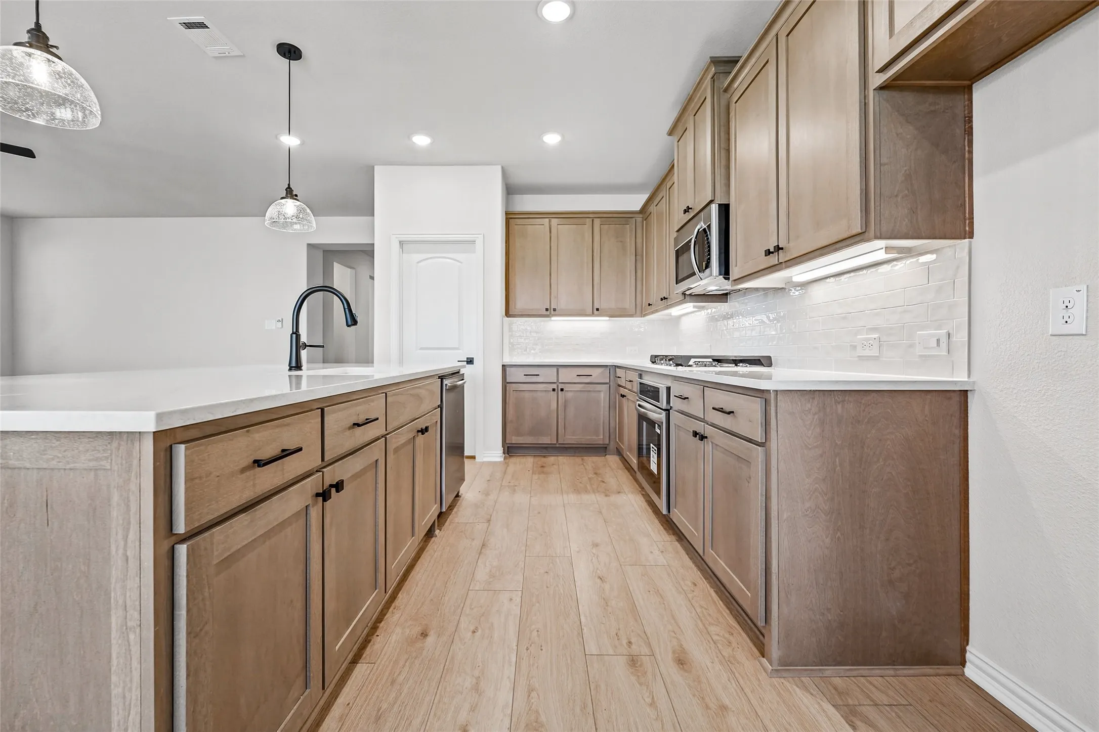 Kitchen featuring wood-finish flooring, light-toned cabinetry, a large center island with a sink, white countertops, and stainless steel appliances