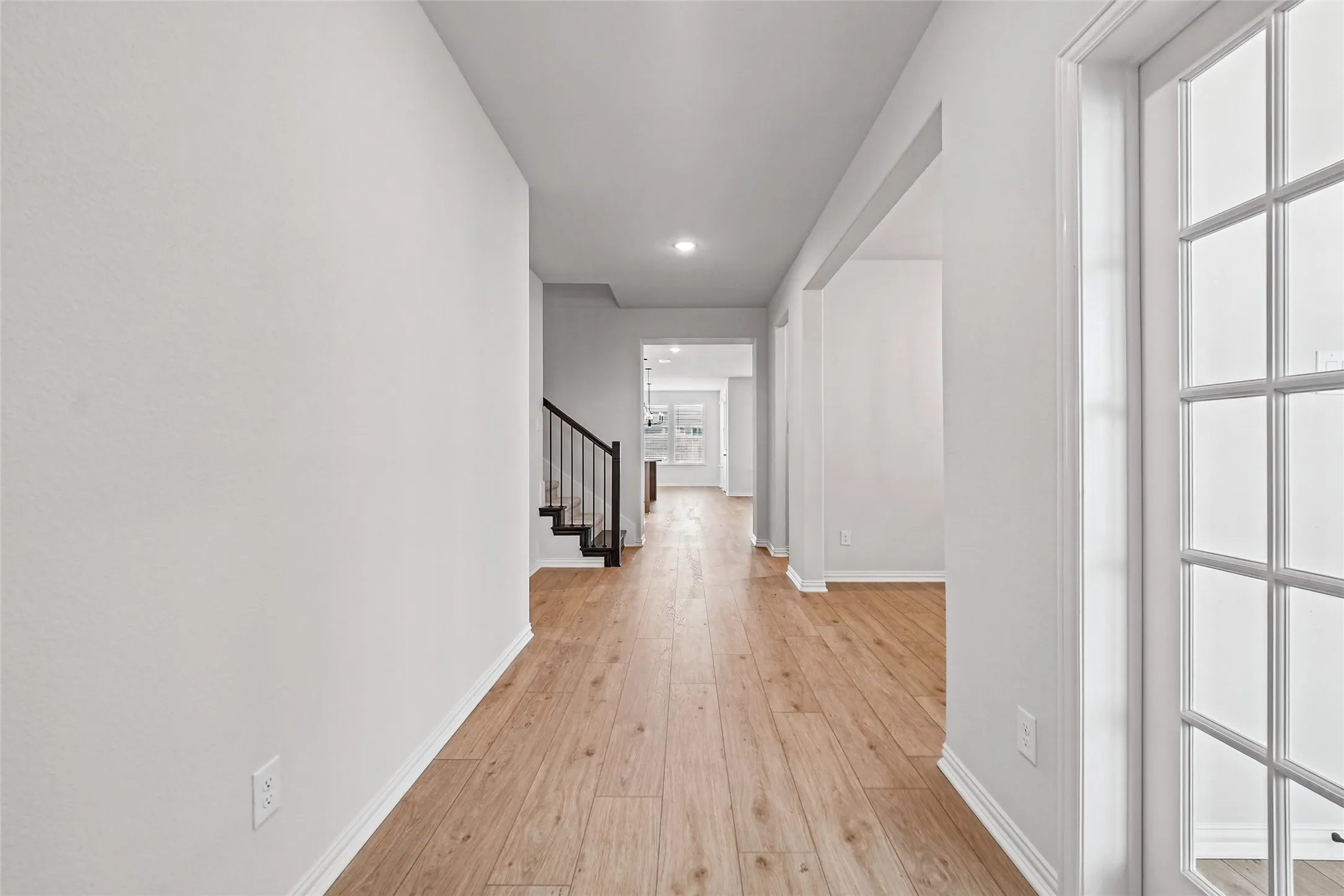 Hallway featuring wood-finish flooring, recessed lighting, and a staircase with dark wood treads and metal balusters