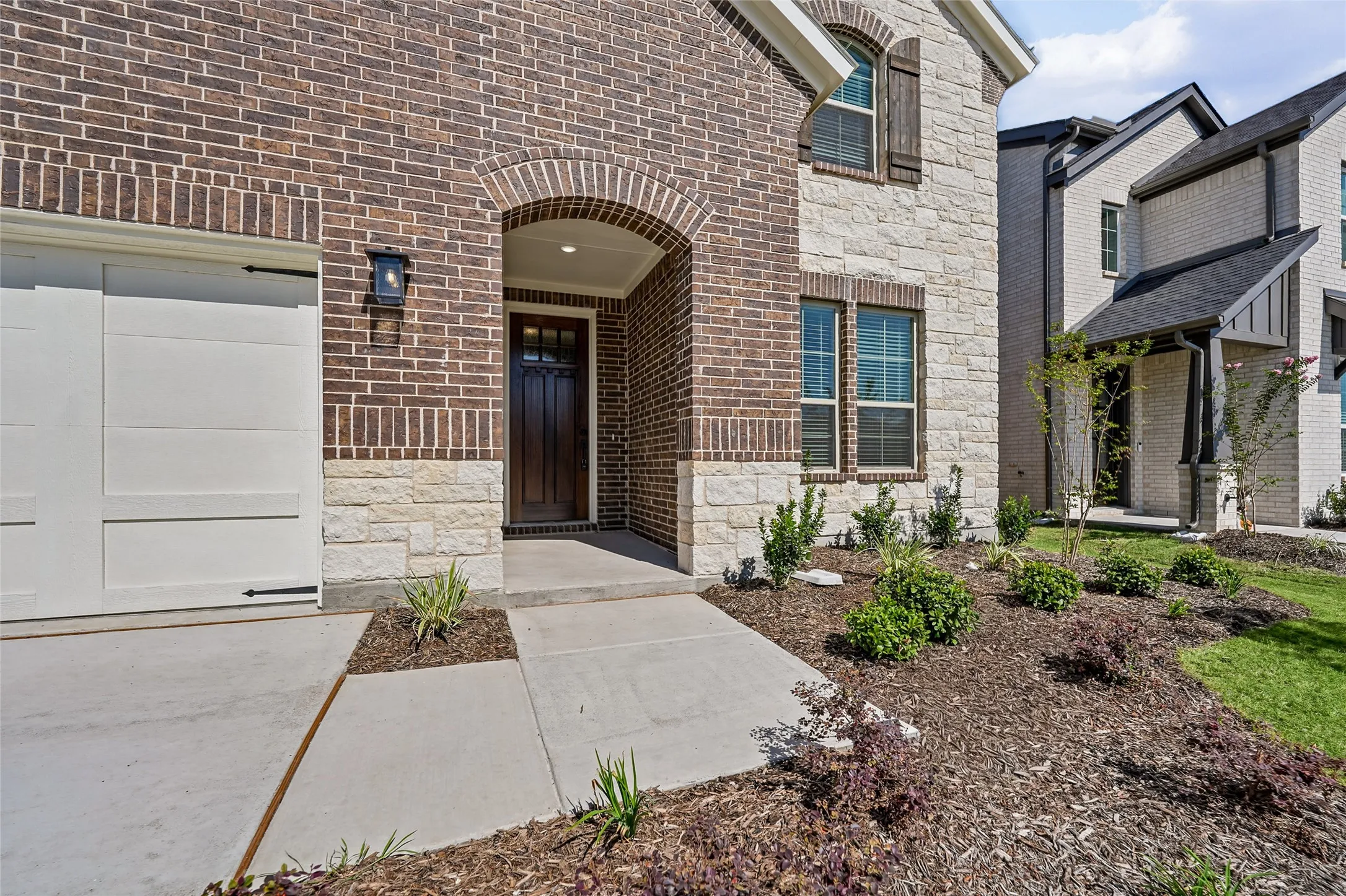Brick and stone facade with an arched entryway, decorative garage door, and established landscaping