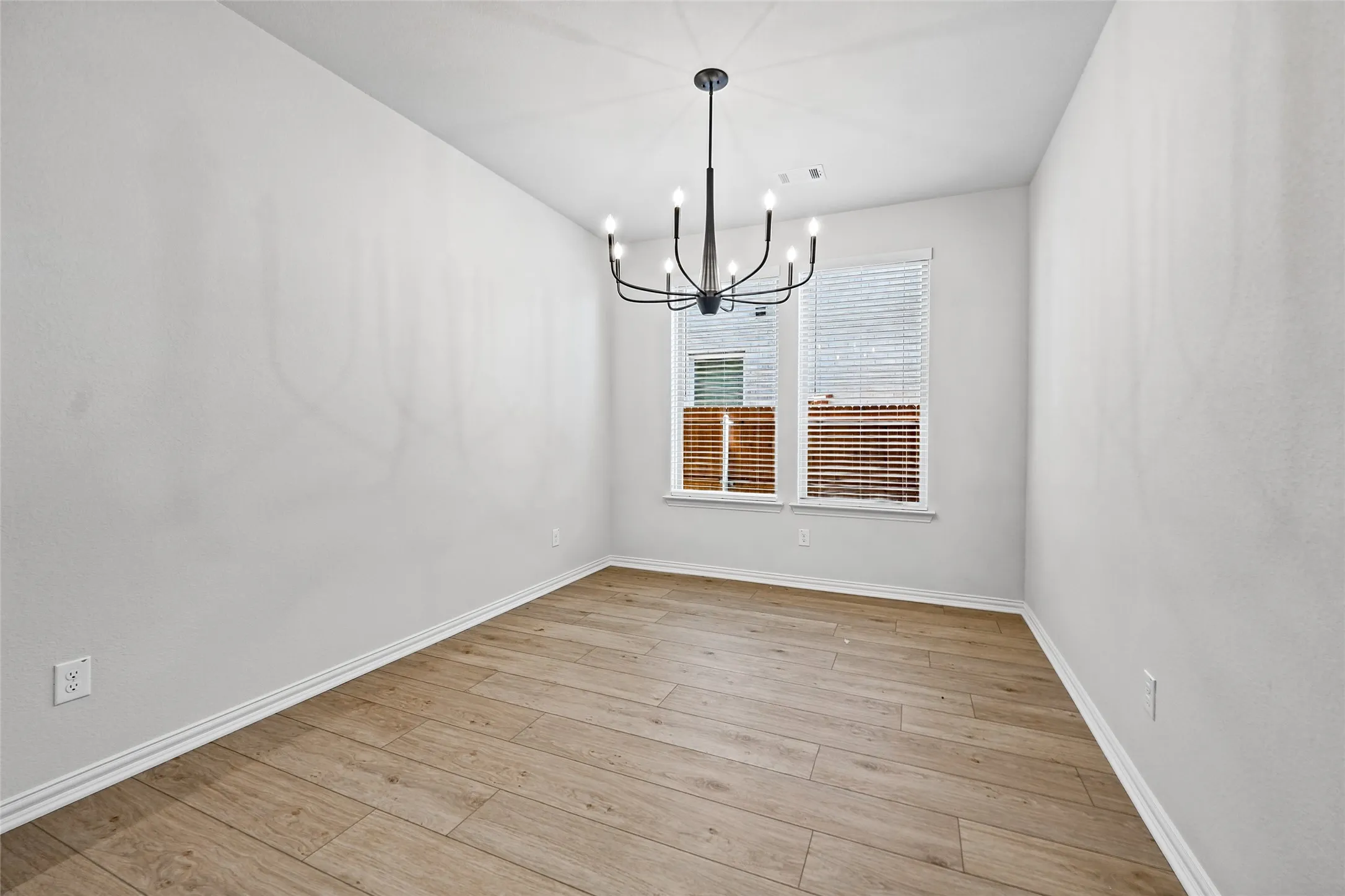 Wood-finish flooring, white painted walls, and a modern black chandelier
