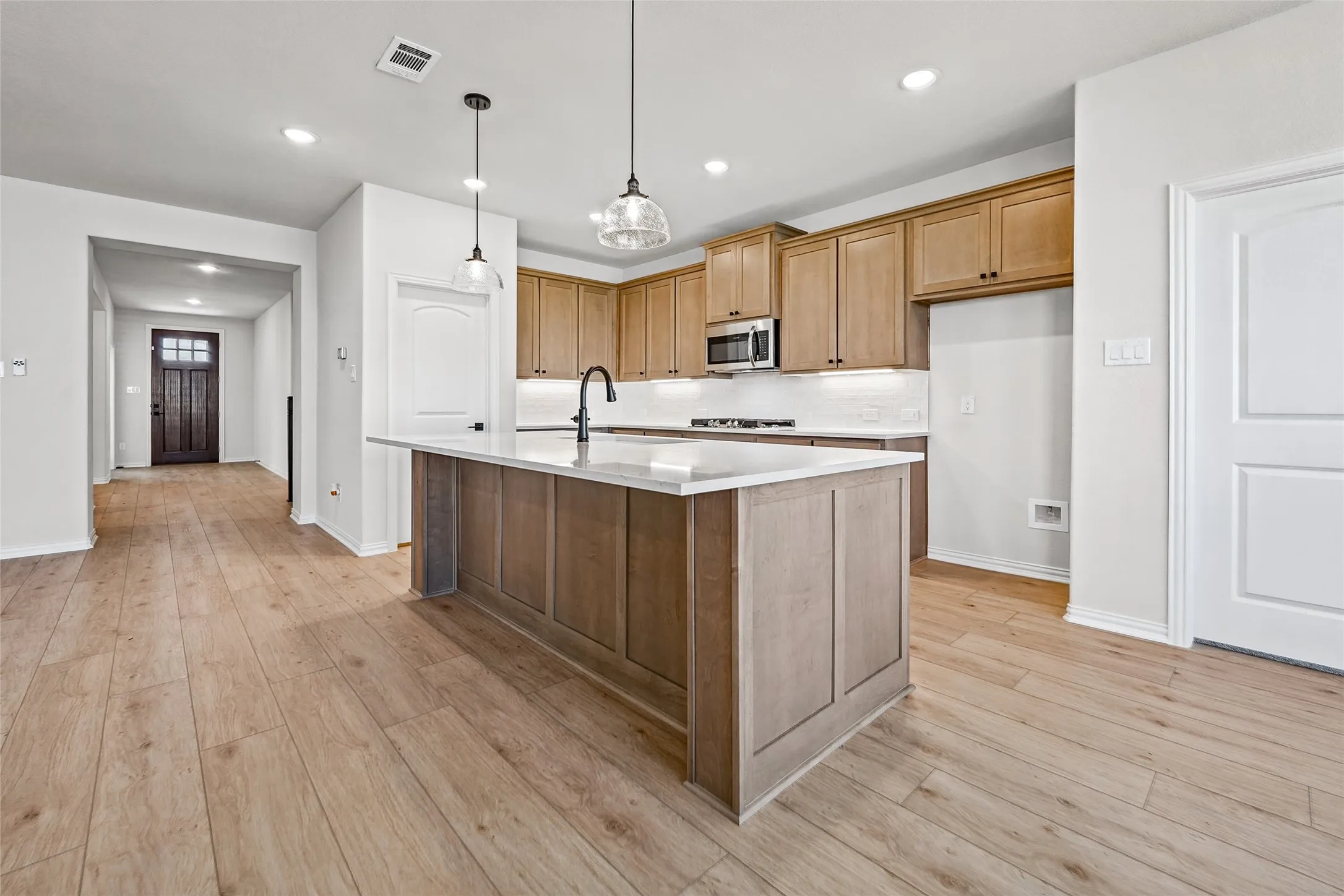 Open-concept kitchen with a central island, light wood-finish flooring, recessed lighting, and pendant fixtures
