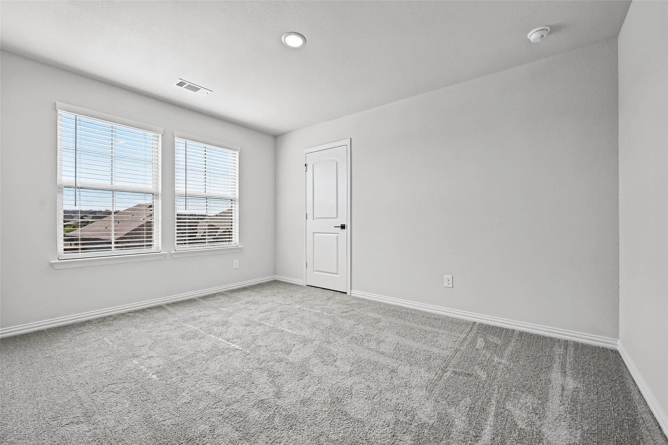 Carpeted flooring, recessed lighting, dual windows with blinds, and white door with black hardware