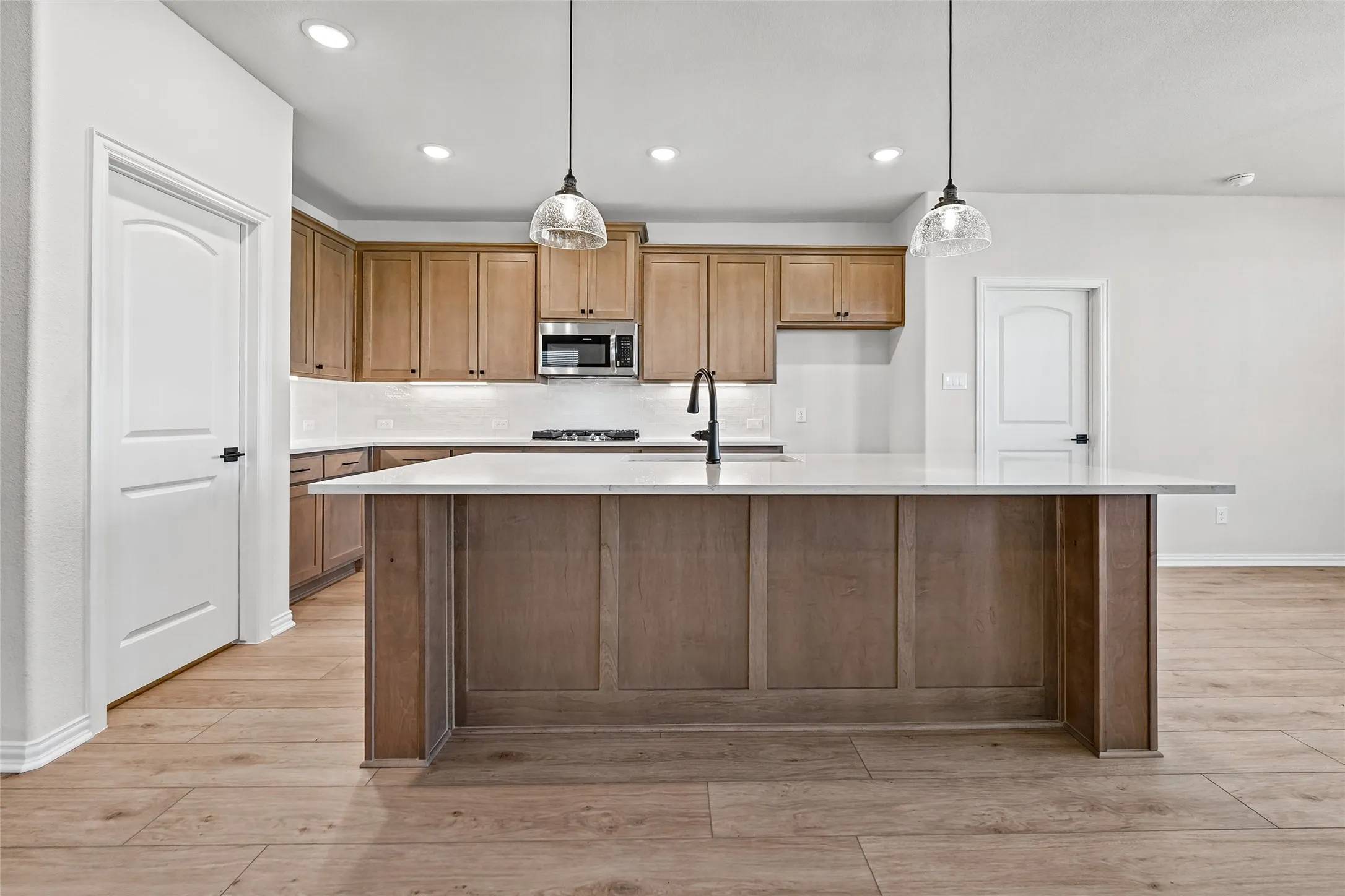 Spacious kitchen island with a light-toned countertop, wood-finish flooring, recessed lighting, and pendant light fixtures