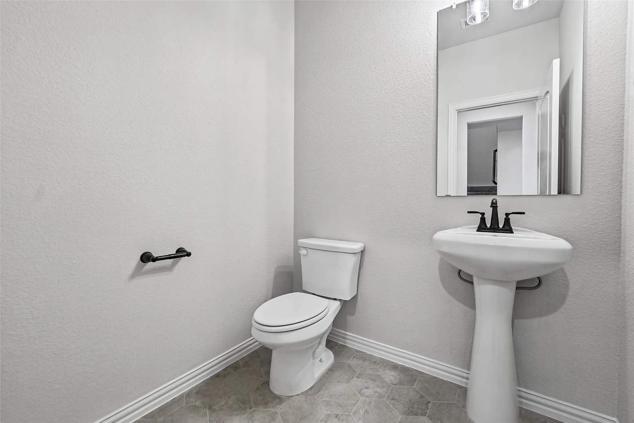 Half bath featuring a pedestal sink with matte black faucet, a two-piece toilet with elongated bowl, and a framed mirror with integrated lighting