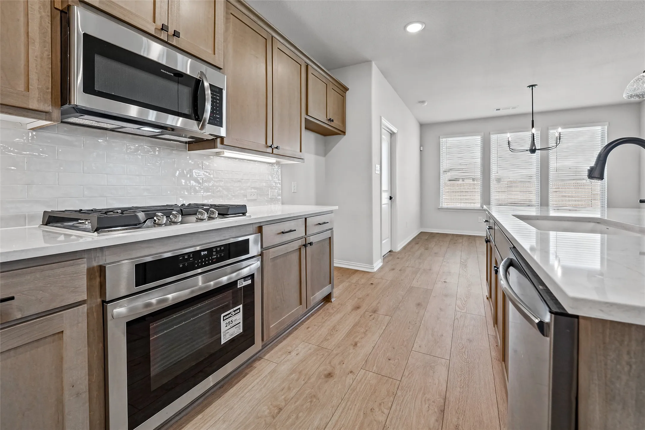 Kitchen featuring stainless steel appliances, wood-finish flooring, light-toned cabinetry, white subway tile backsplash, and a large sink with a gooseneck faucet