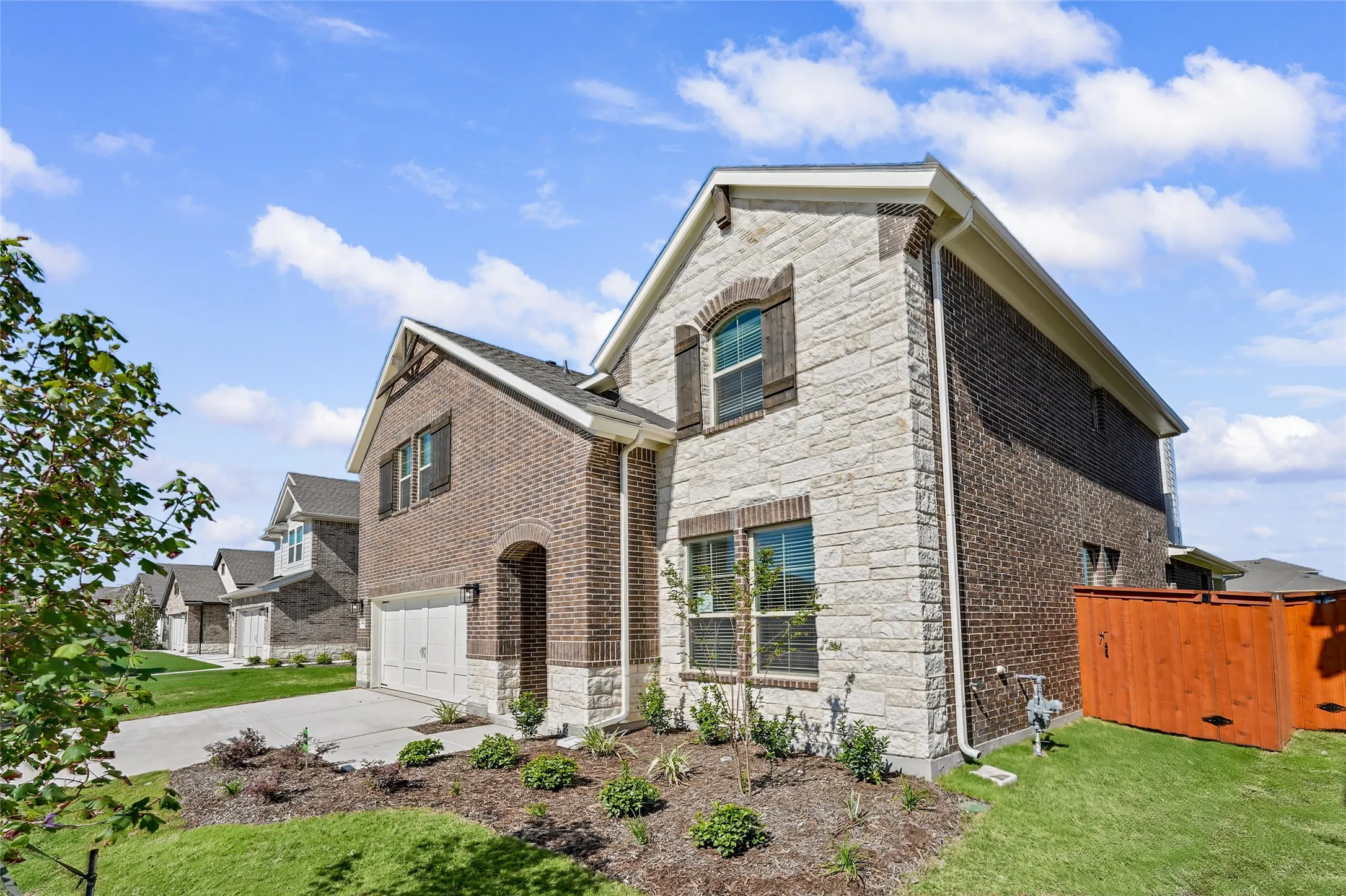 Stone and brick exterior with wood-finish shutters, arched entry, and an attached two-car garage