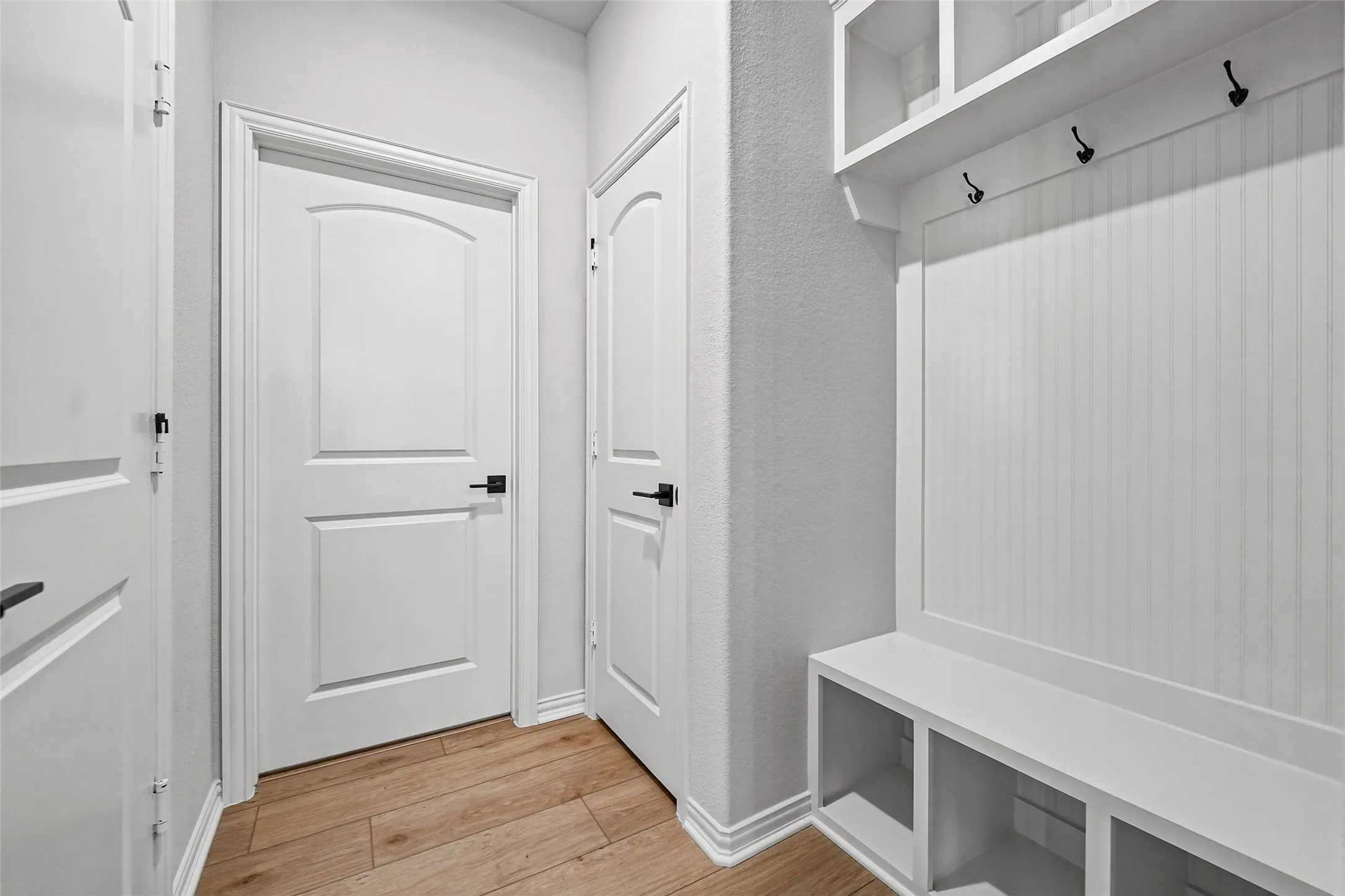 Built-in mudroom storage with beadboard backing, integrated bench seating, three storage cubbies, and overhead shelving with coat hooks