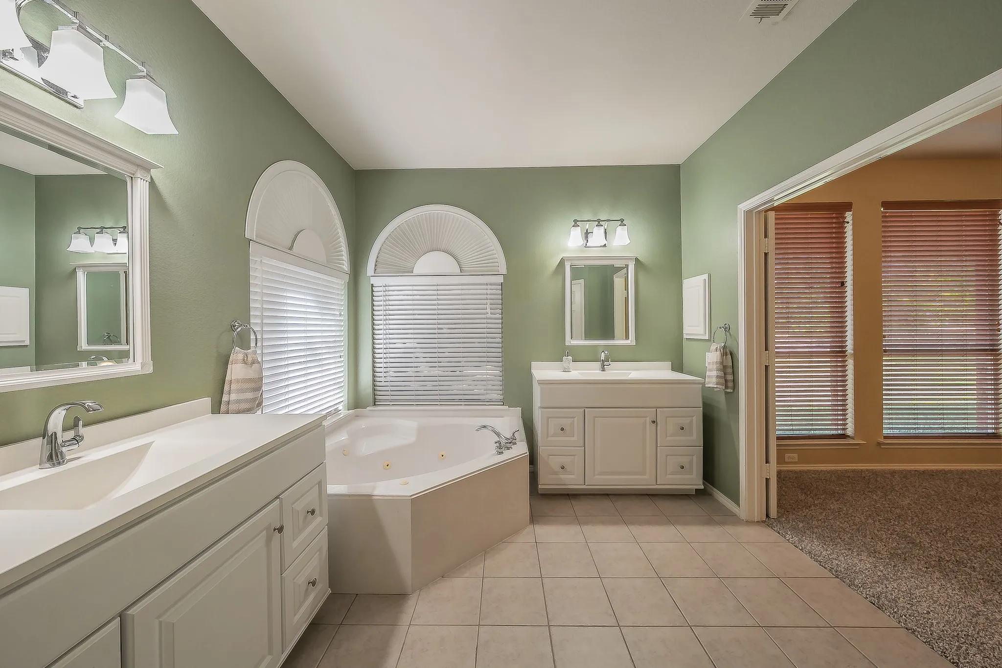 Bathroom featuring dual vanities with white cabinetry, a corner built-in soaking tub, and tile flooring