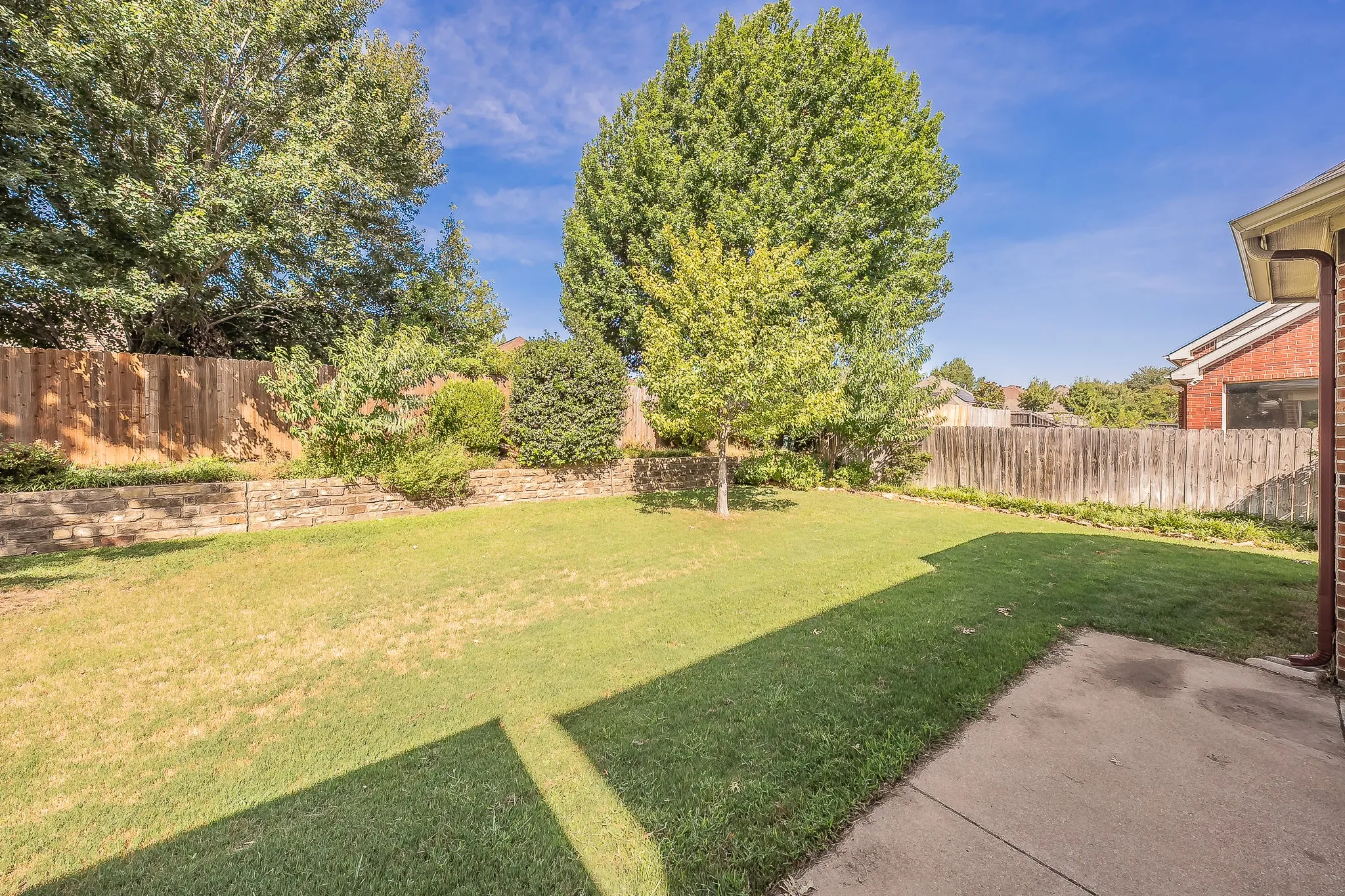 Expansive backyard featuring a manicured lawn, mature trees, and a stone retaining wall