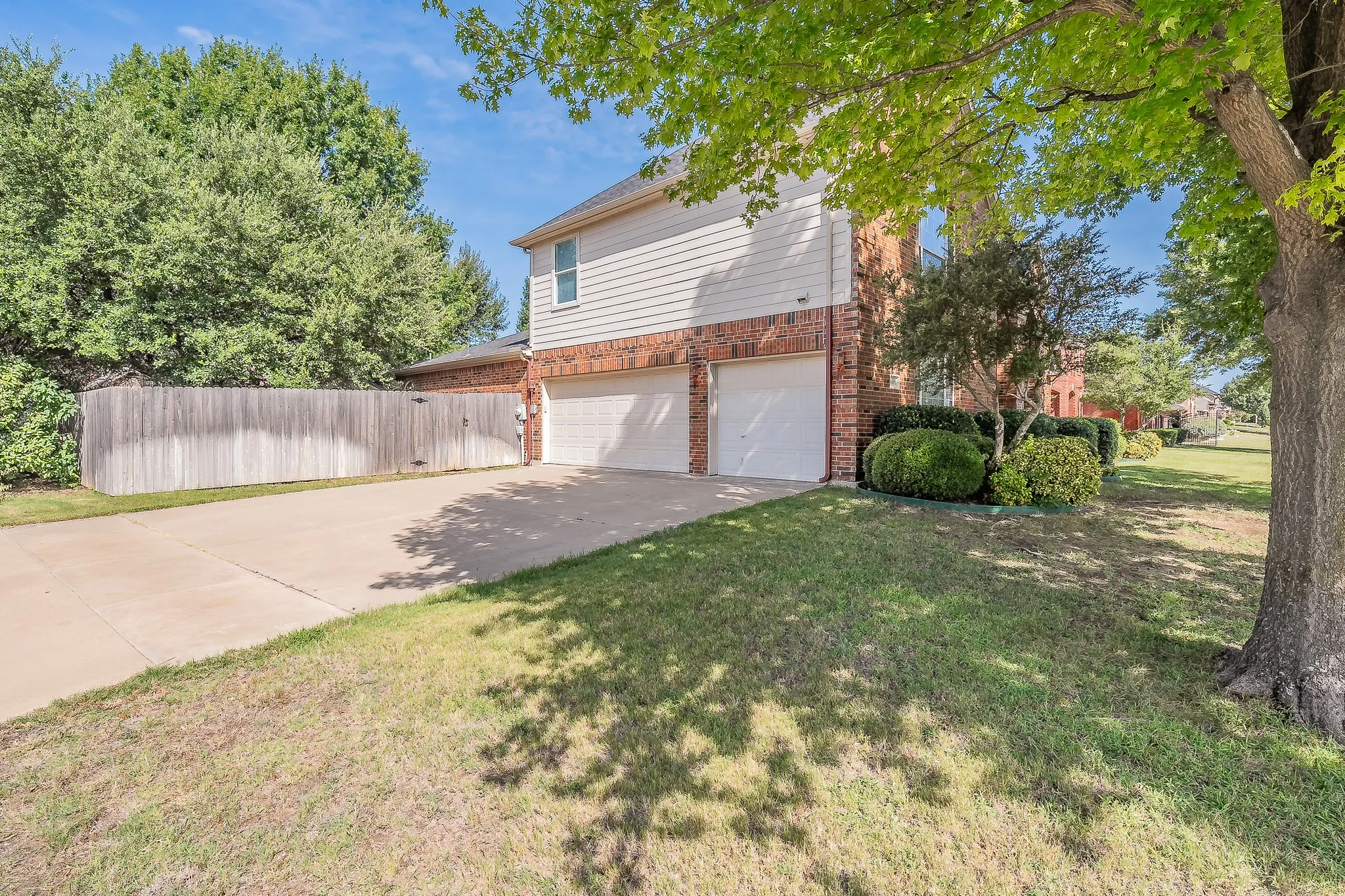 Three-car garage with white garage doors, brick and siding exterior, concrete driveway, and established landscaping
