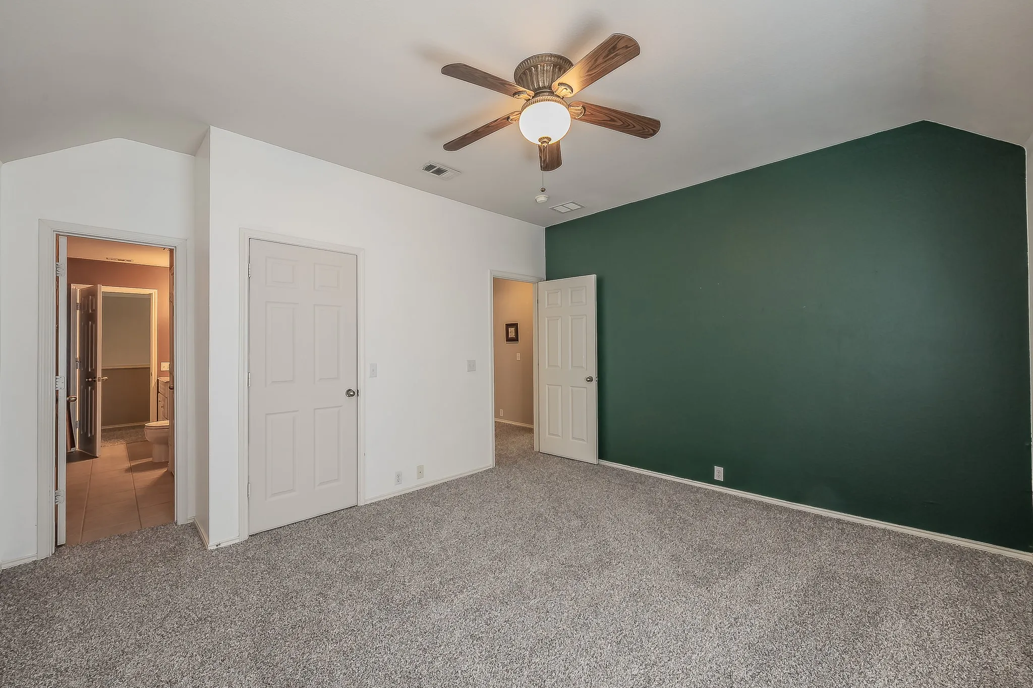 Bedroom featuring plush gray carpeting, a dark green accent wall, and a ceiling fan with light fixture