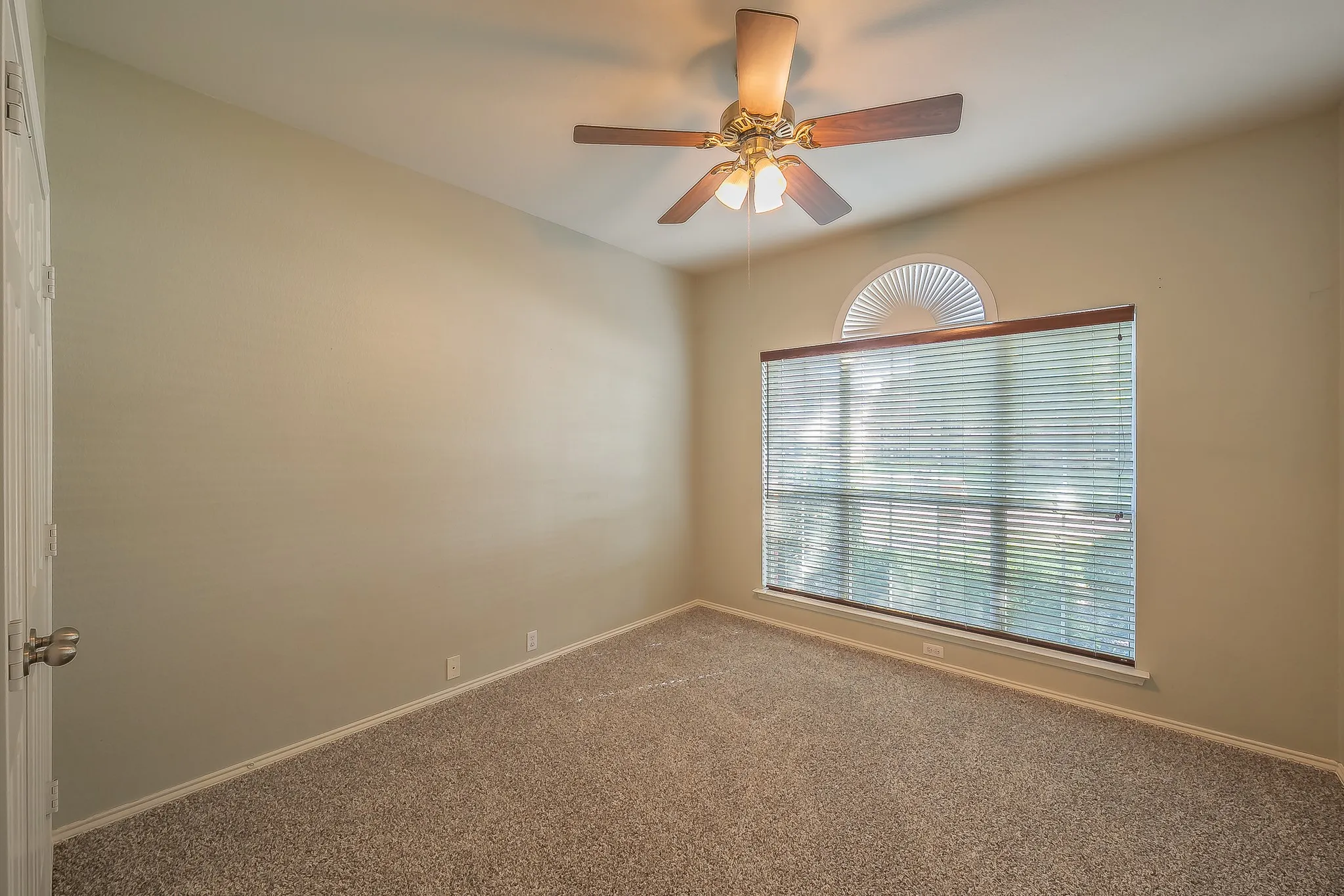 Neutral-toned room featuring a large window with blinds and an arched transom