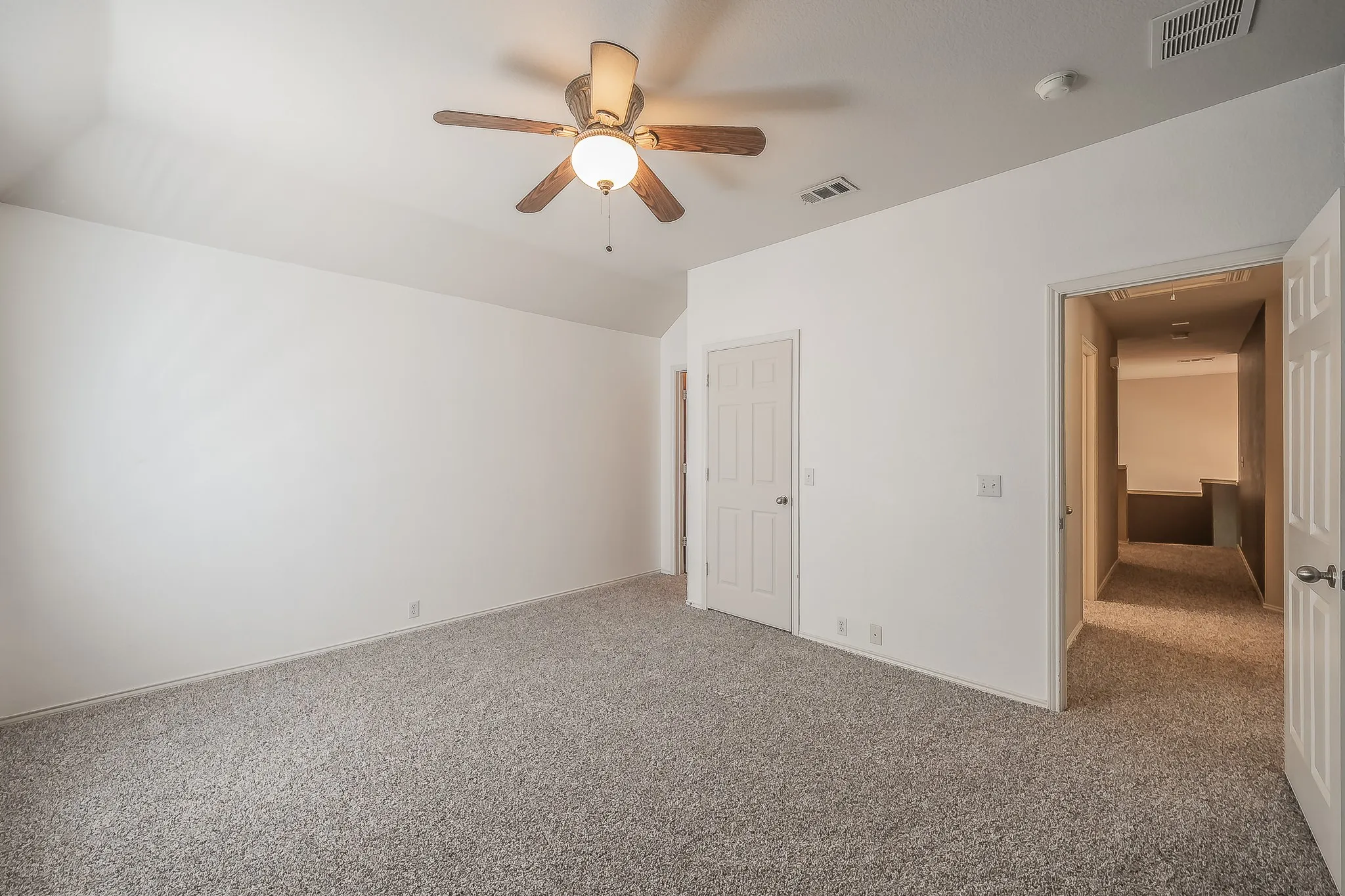 Spacious room with sloped ceiling, wood-finish ceiling fan, and light gray carpet