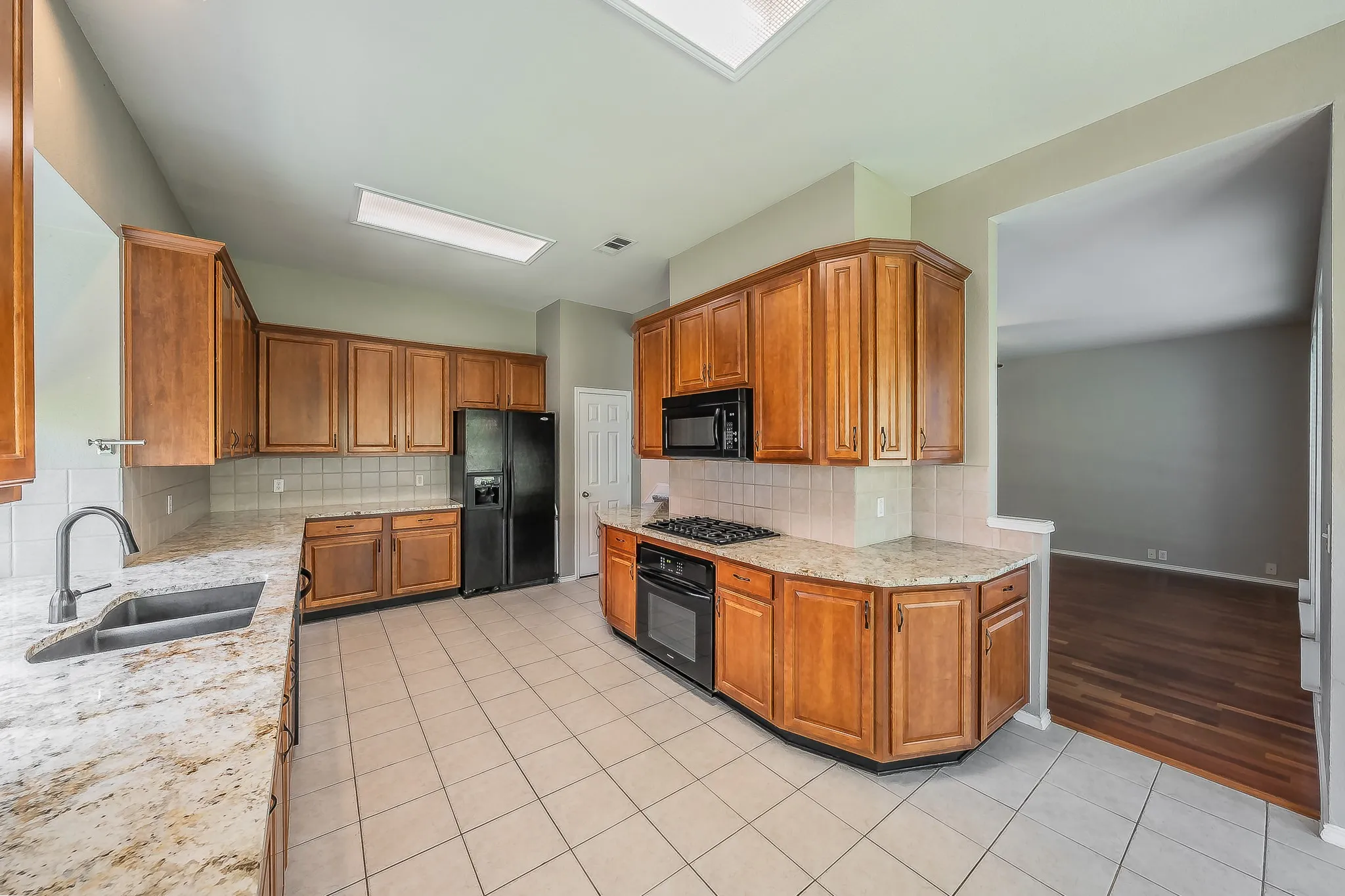 Spacious kitchen featuring light wood cabinetry, stone-finish countertops, and a tile backsplash