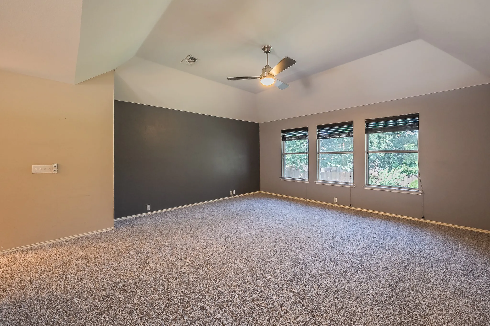 Spacious room featuring vaulted ceilings, a ceiling fan with integrated lighting, and three large windows