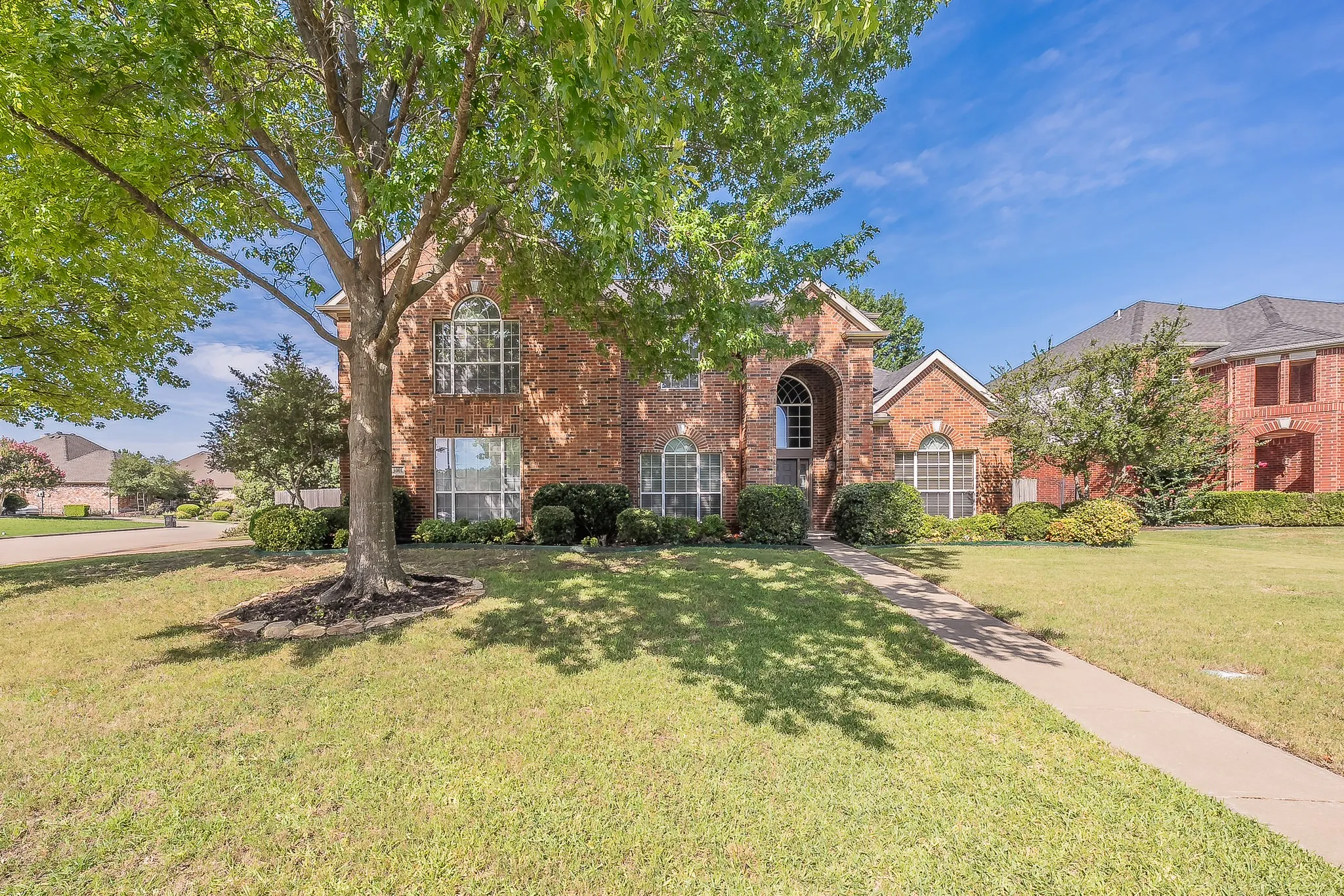 Traditional brick exterior featuring a mature tree, arched entryway, and multiple large windows