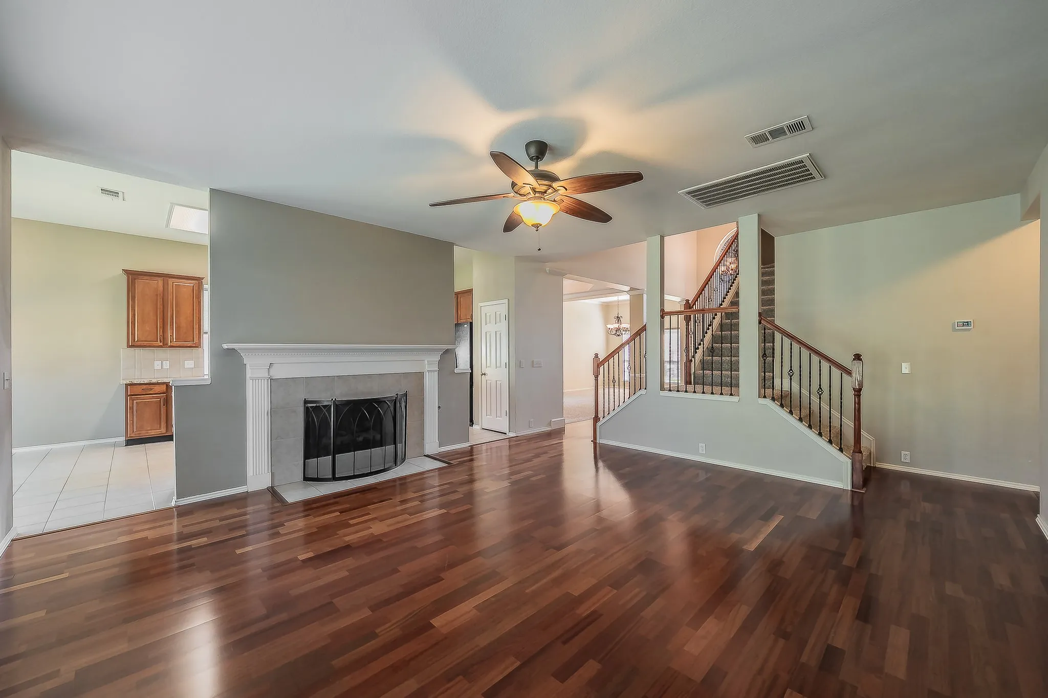 Spacious interior featuring wood-finish flooring, a ceiling fan with integrated lighting, a fireplace with a mantel, and a staircase with wrought iron balusters