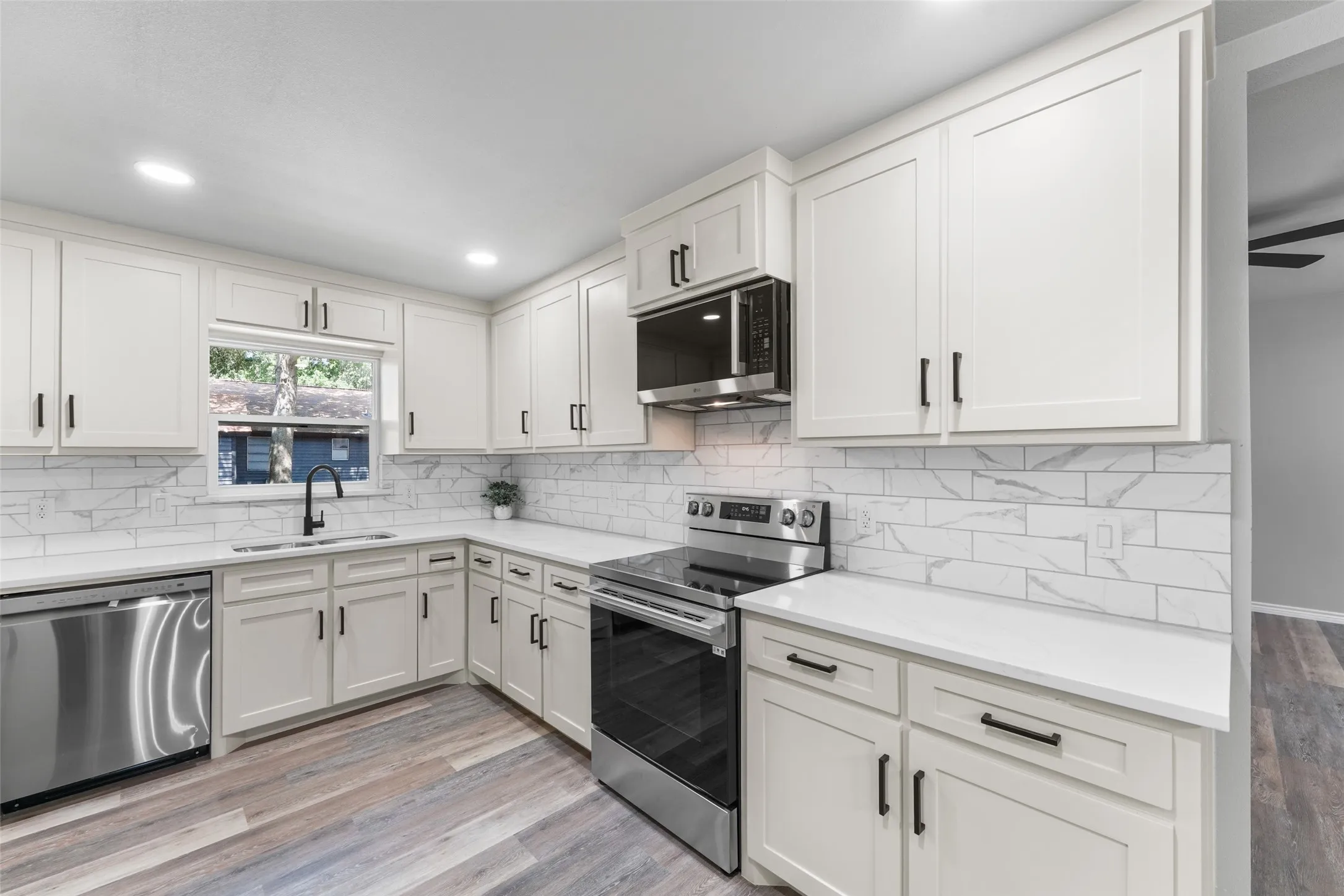 Modern kitchen featuring white shaker cabinetry, stainless steel appliances, white subway tile backsplash, light wood-finish flooring, and recessed lighting