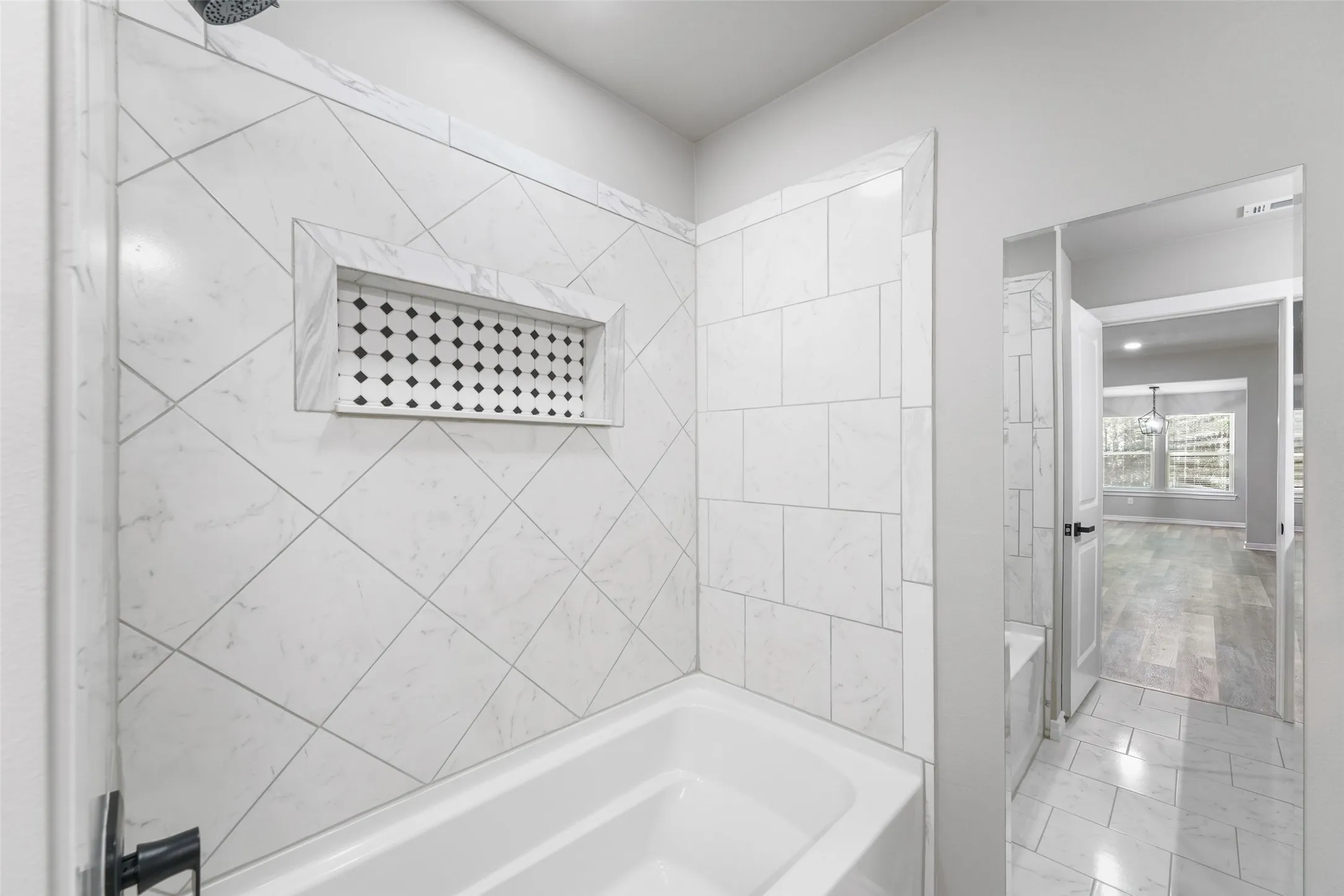White ceramic tile bathtub surround with a decorative niche and black and white patterned tile insert, contrasting black shower fixtures, and light gray wall paint