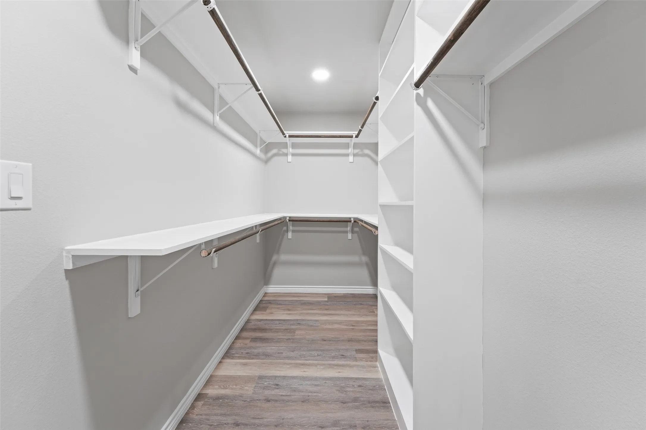 Spacious walk-in closet featuring wood-finish flooring, recessed lighting, white built-in shelving, and multiple hanging rods