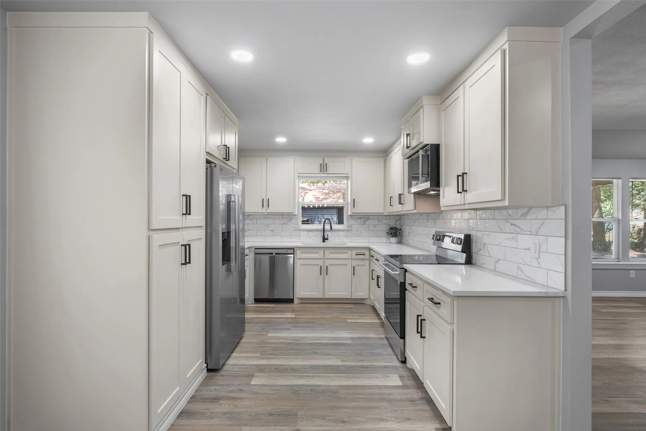 Galley kitchen featuring light shaker cabinetry, light countertops, subway tile backsplash, stainless steel appliances, and wood-finish flooring