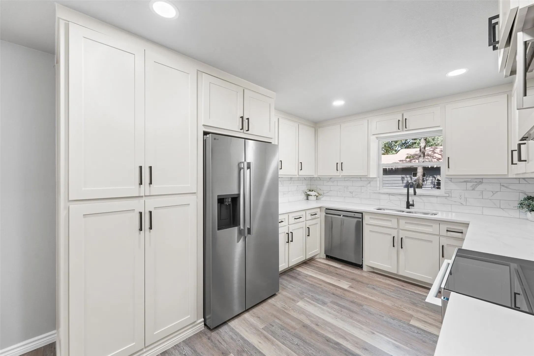 Modern kitchen featuring white shaker cabinetry, stainless steel appliances, wood-finish flooring, white countertops, and a subway tile backsplash