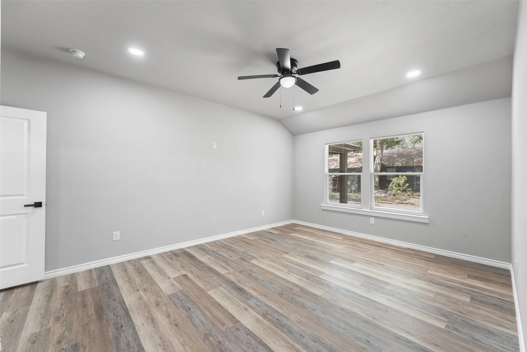 Spacious room featuring wood-finish flooring, light grey walls, and a contemporary ceiling fan